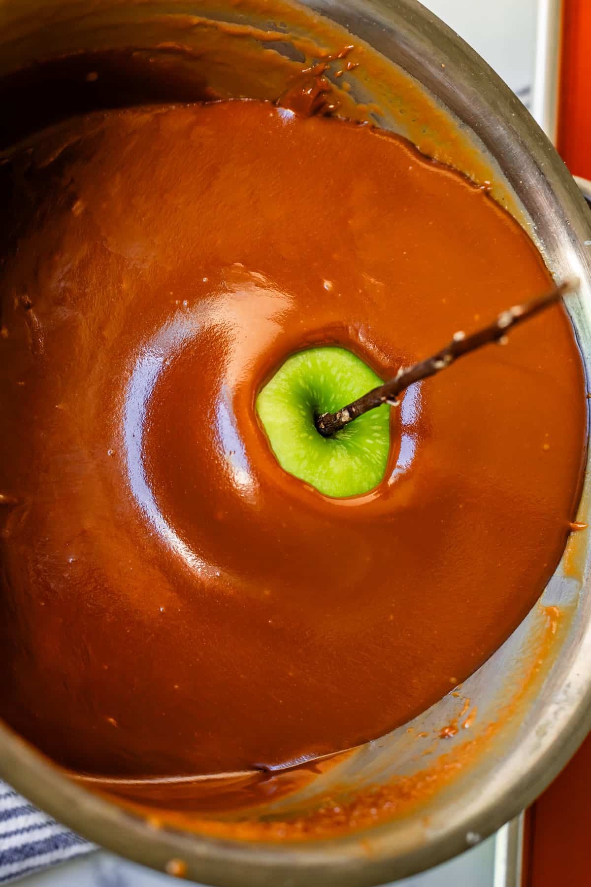 pan tilted and apple with stick in it completely submerged in caramel.