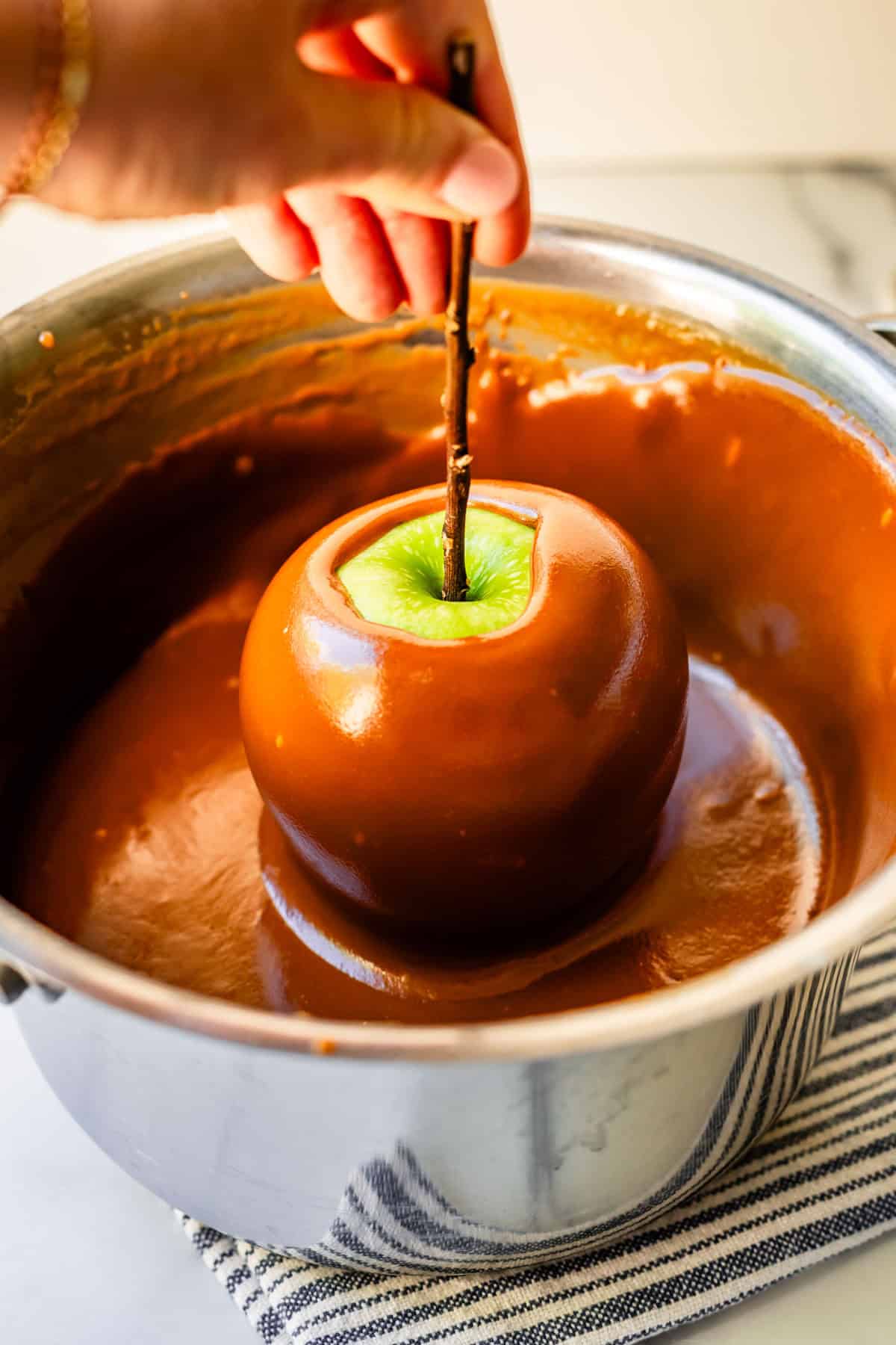 hand lifting out a fully caramel coated granny smith apple from pot.