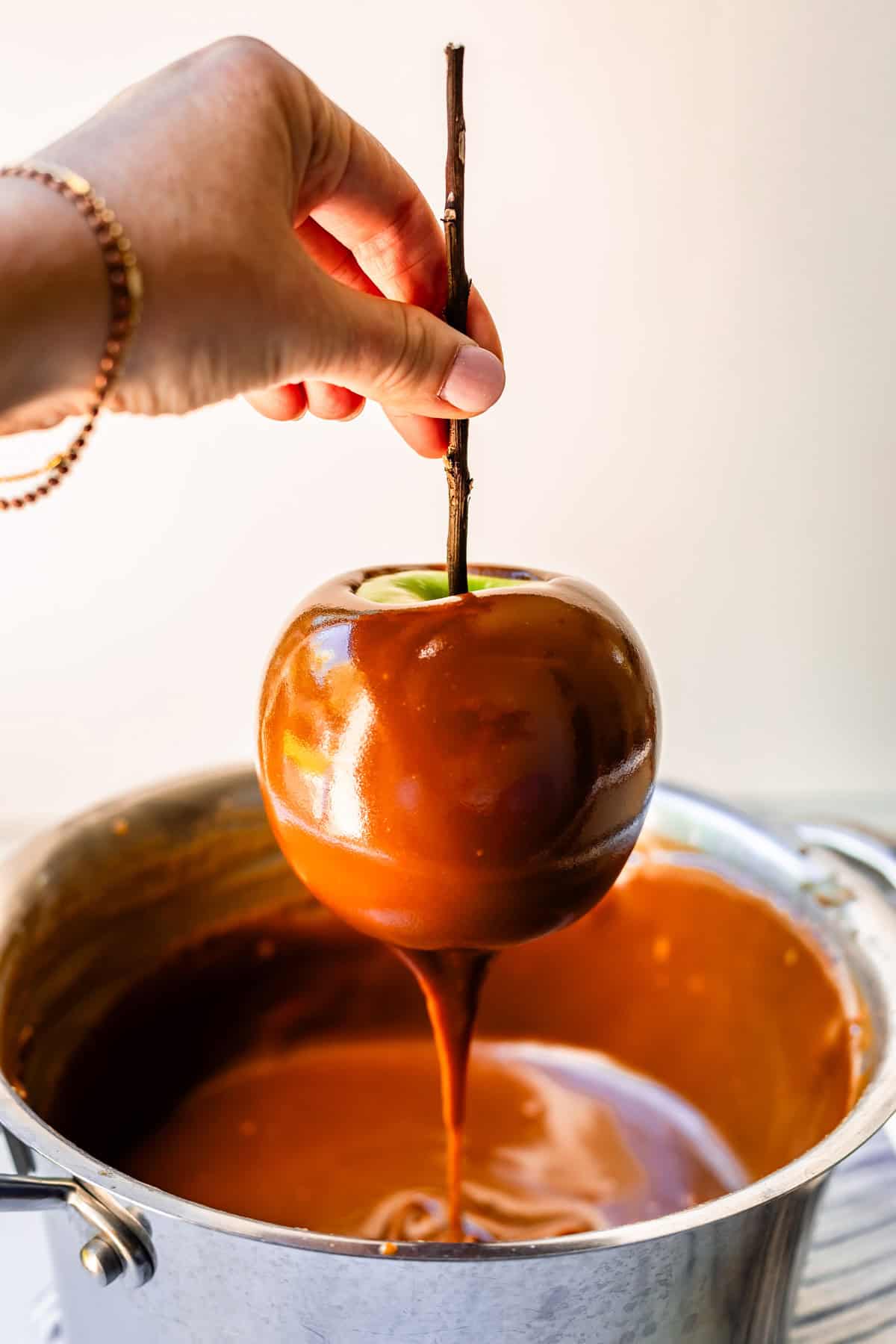 hand holding apple above the pot, letting the excess caramel drip down.