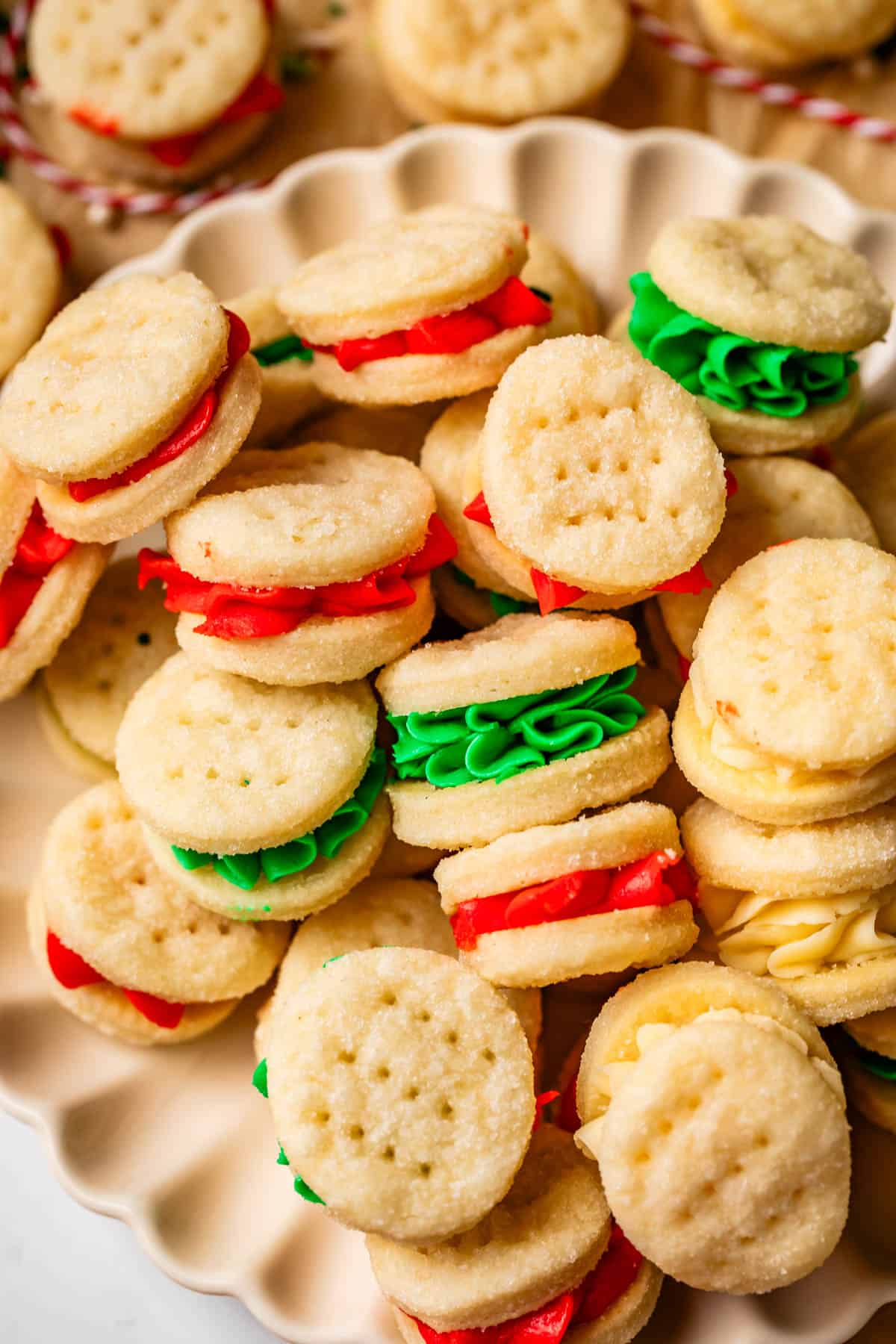 a fluted serving tray with red and green buttercream stuffed cream wafer cookie sandwiches.