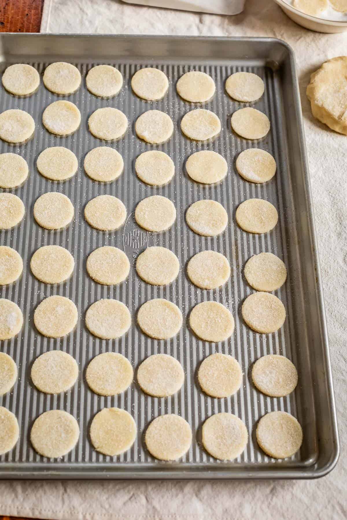 a metal sheet pan with several dozen small cookie cutouts lined up.