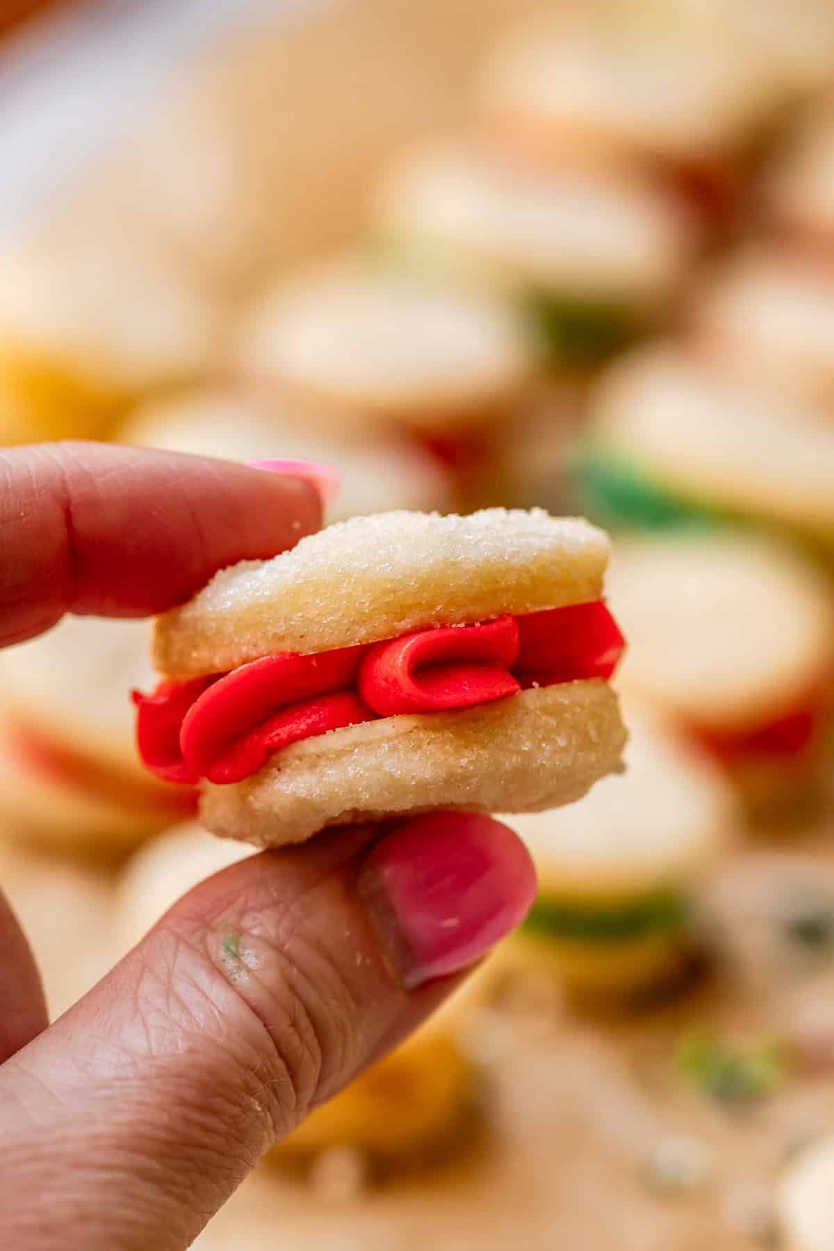 finger and thumb holding up a Swedish cream sandwich wafer filled with red buttercream.