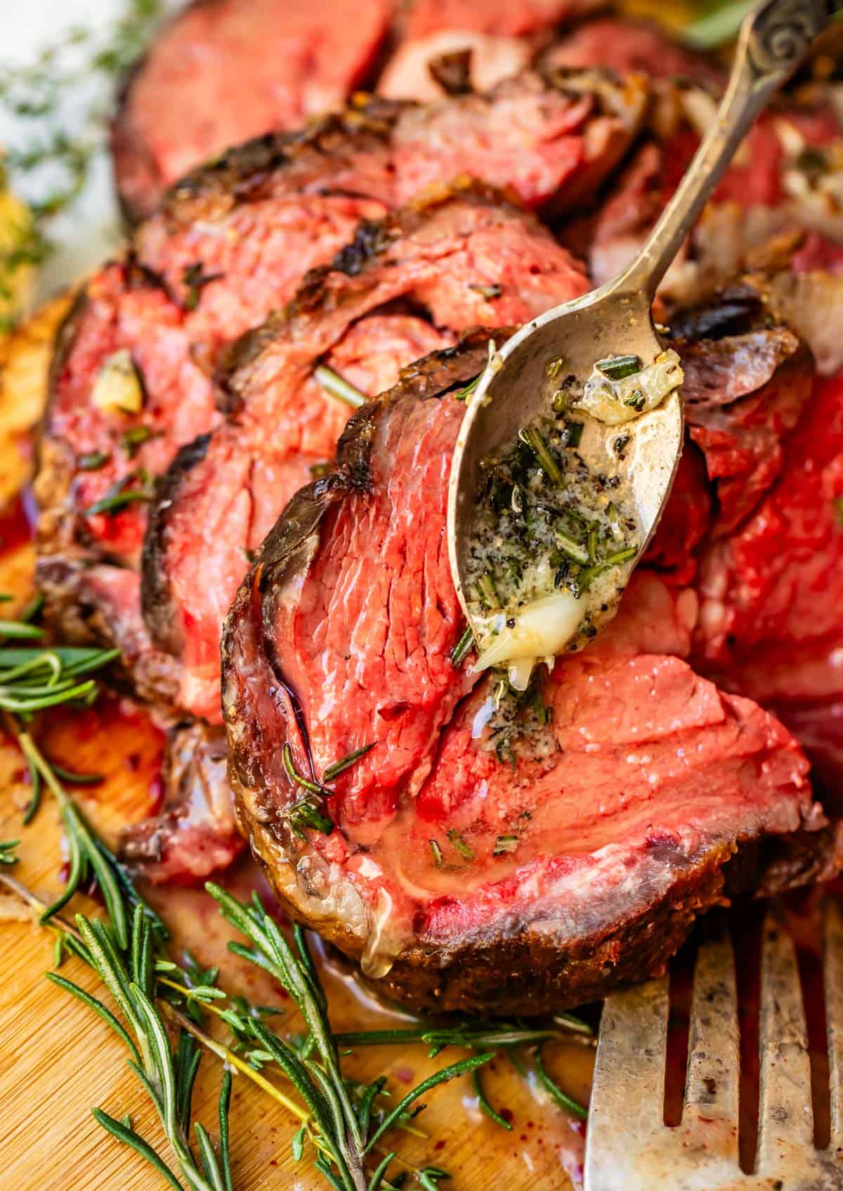 Slices of prime rib leaning against each other on bamboo cutting board with sprigs of thyme.