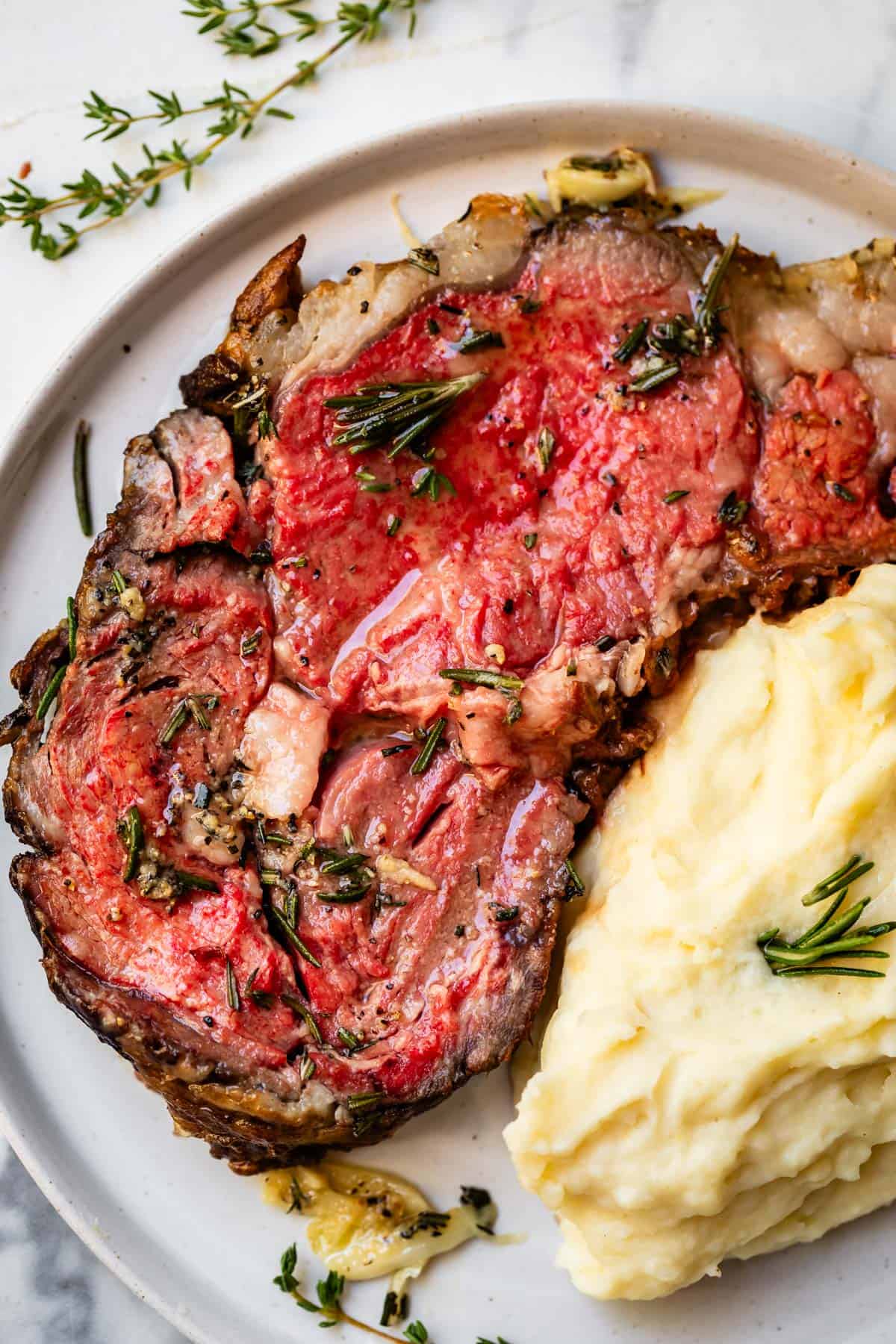 Slice of rare prime rib on plate overhead next to mashed potatoes.