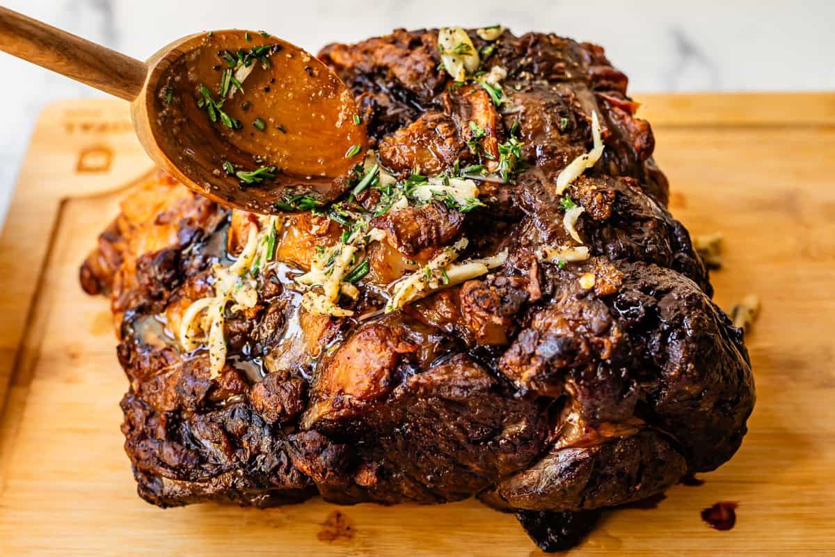 wooden spoon gently pouring garlic butter sauce over the top of the prime rib.