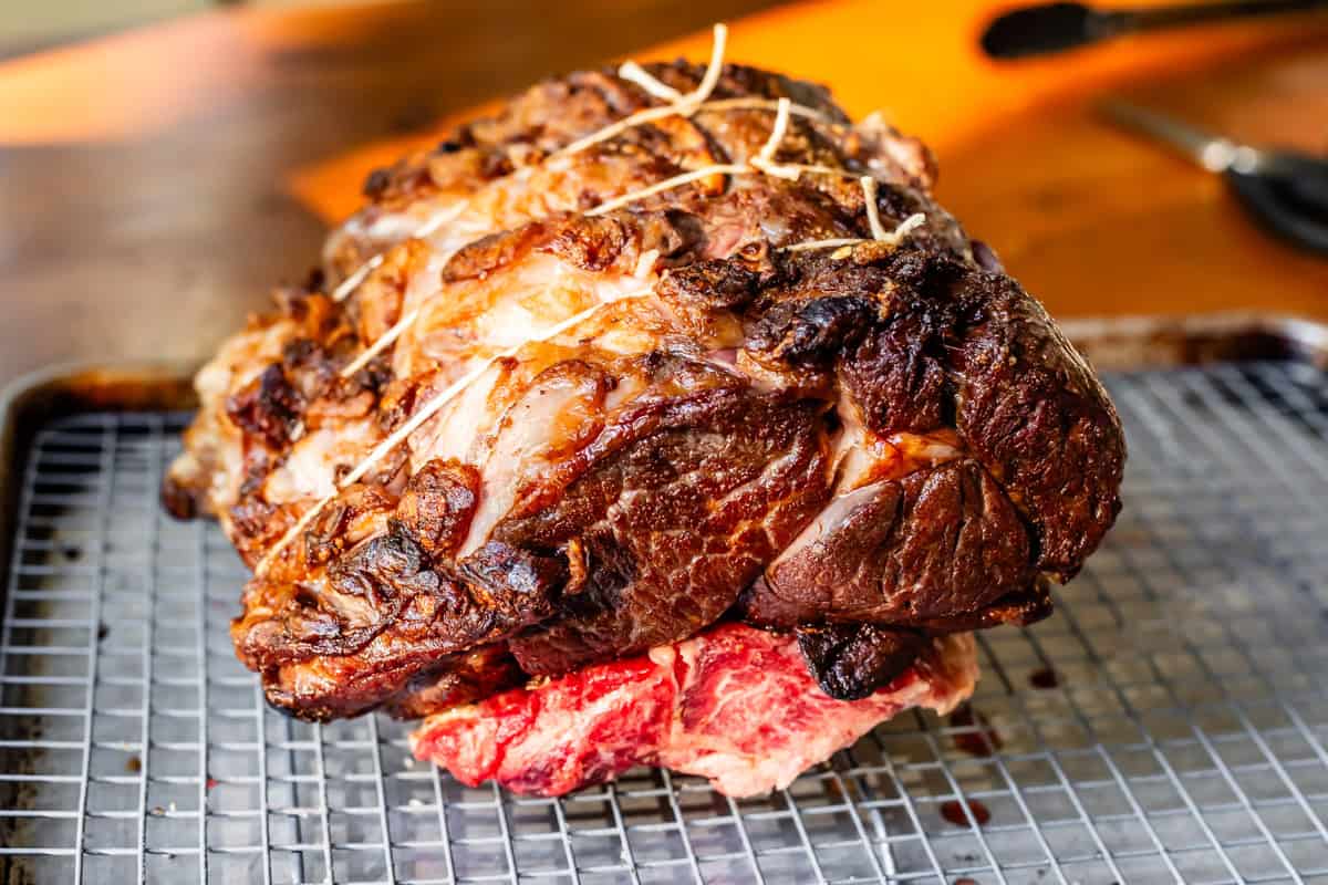 seared ribs tied with twine sitting on top of bones that are on the cooling rack.