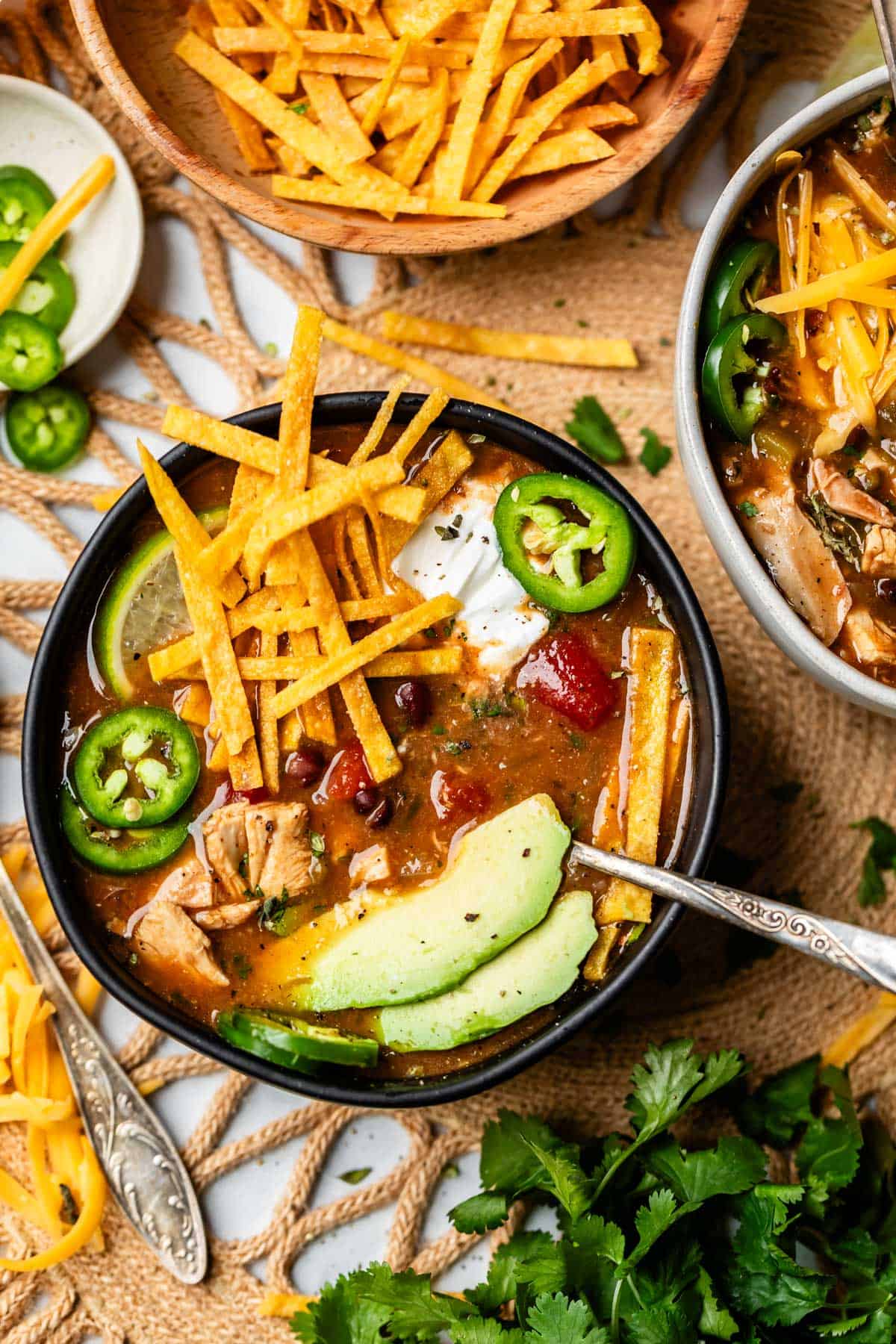 table setting with a few bowls of chicken tortilla soup with toppings.