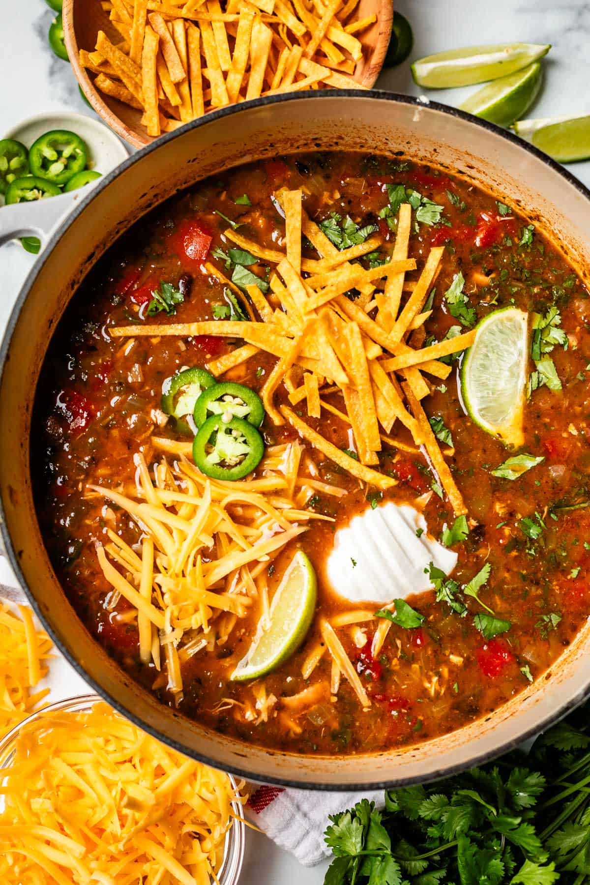 bowl of soup with tortilla strip, cheese, lime, and jalapeno garnish.