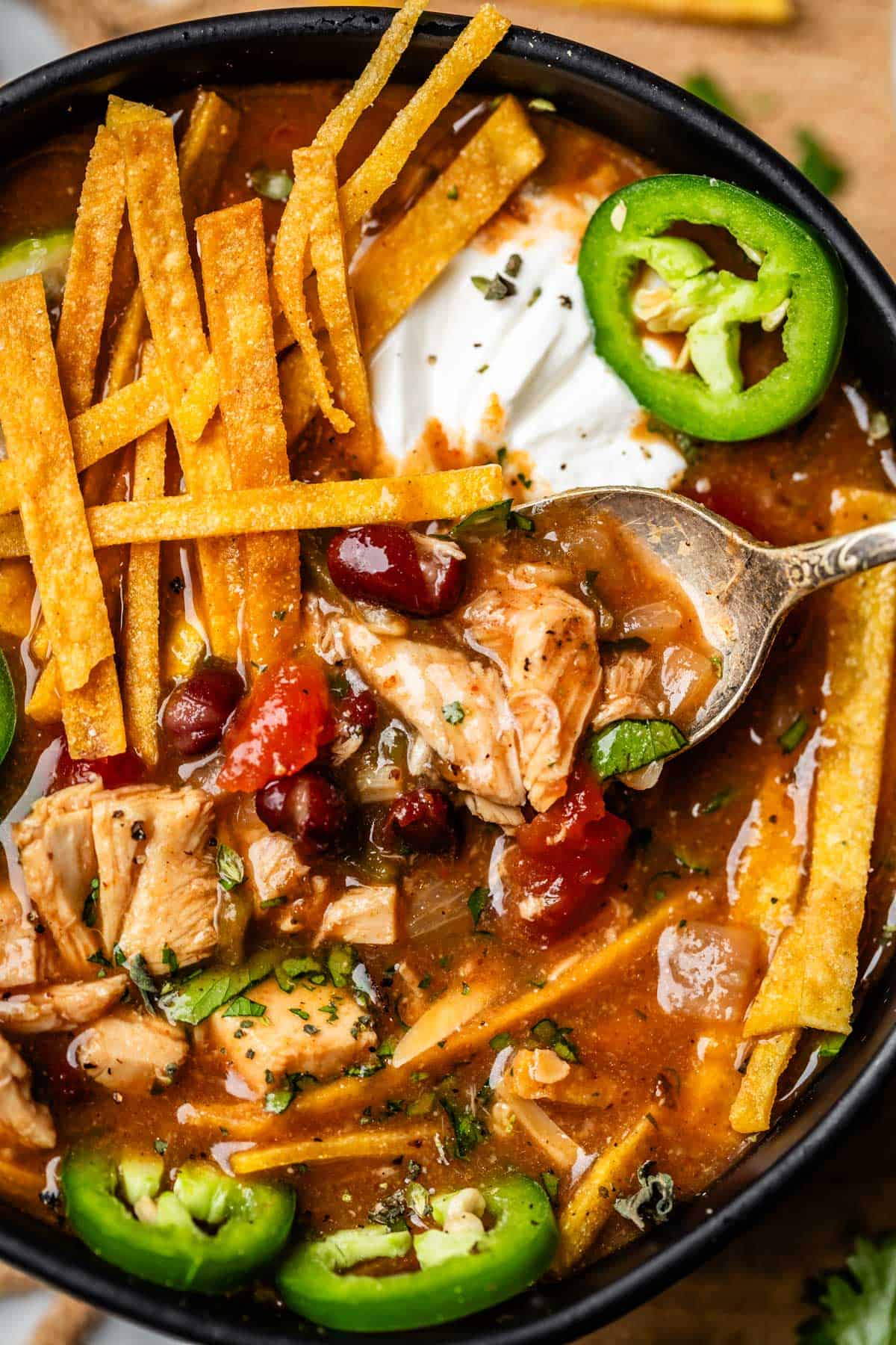 spoon lifting up a bite of chicken filled soup, with fried tortilla and other toppings.