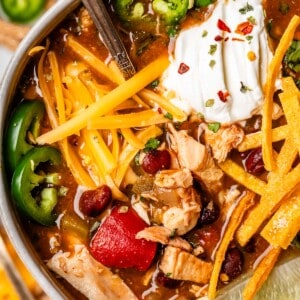 bowl with chicken tortilla soup topped with cheese, sour cream, fried tortilla strips, and more.