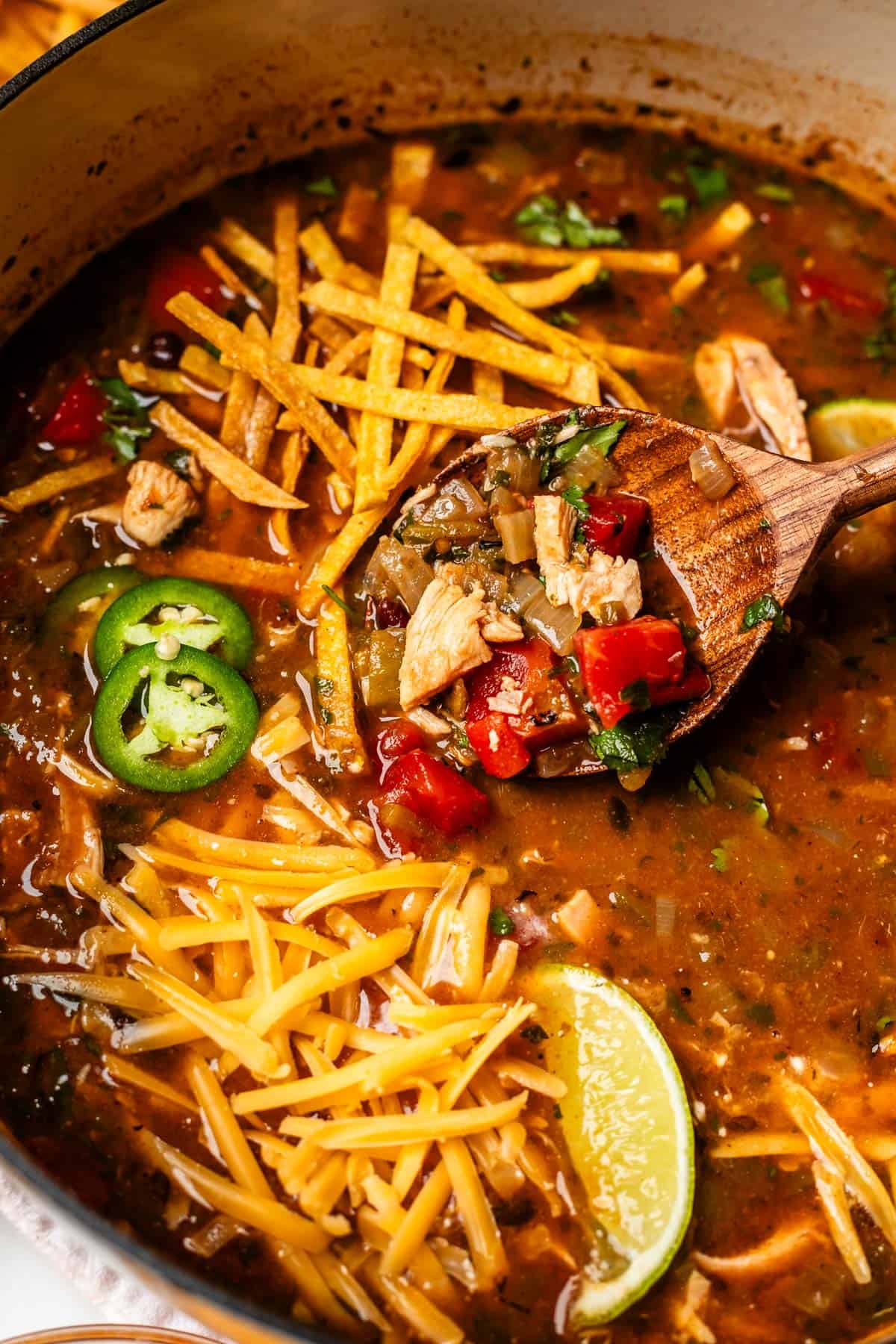 wooden spoon lifting some soup out of a bowl that is garnished with cheese and tortilla.