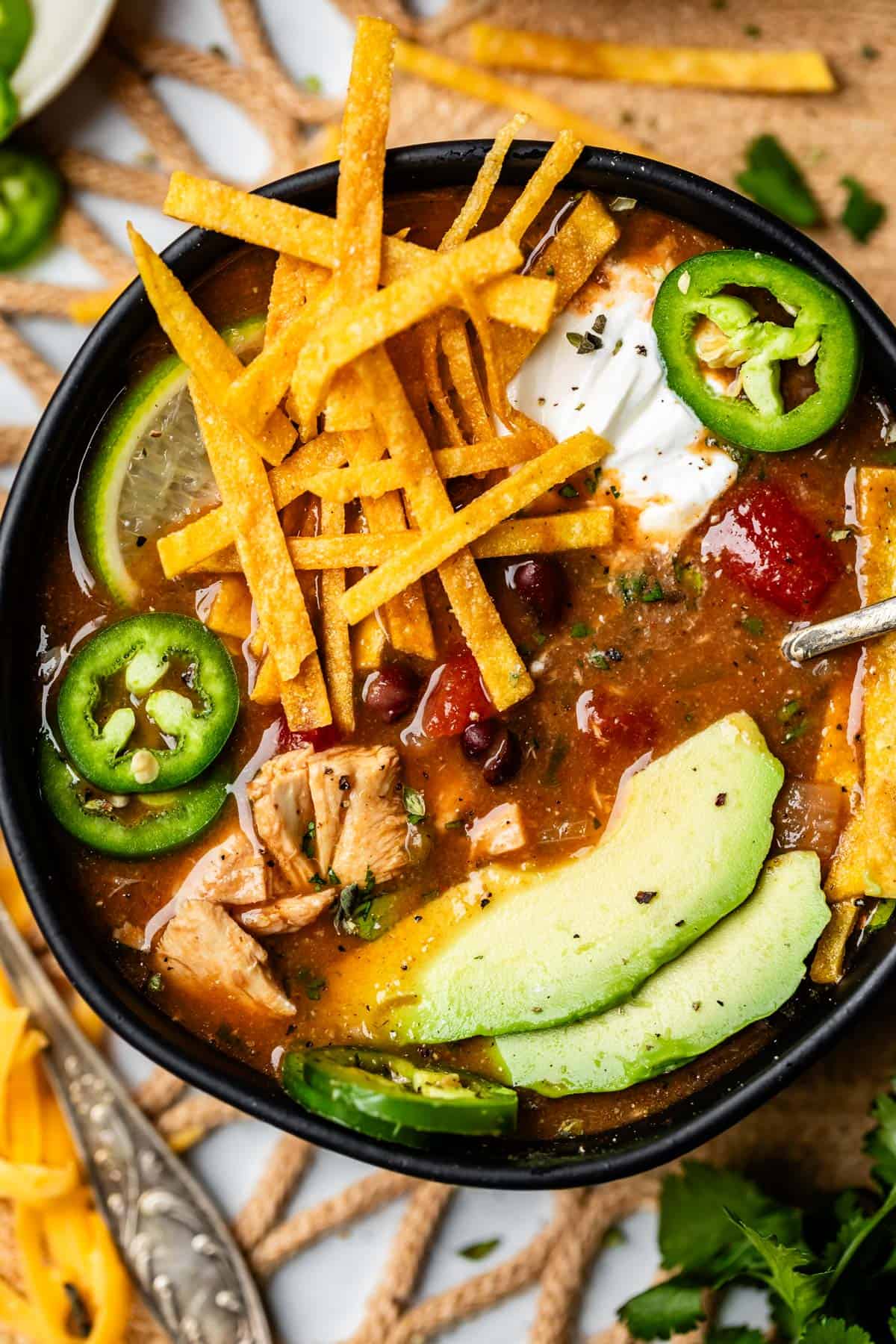 bowl of soup with fried tortilla strips, avocado, and jalapeno.