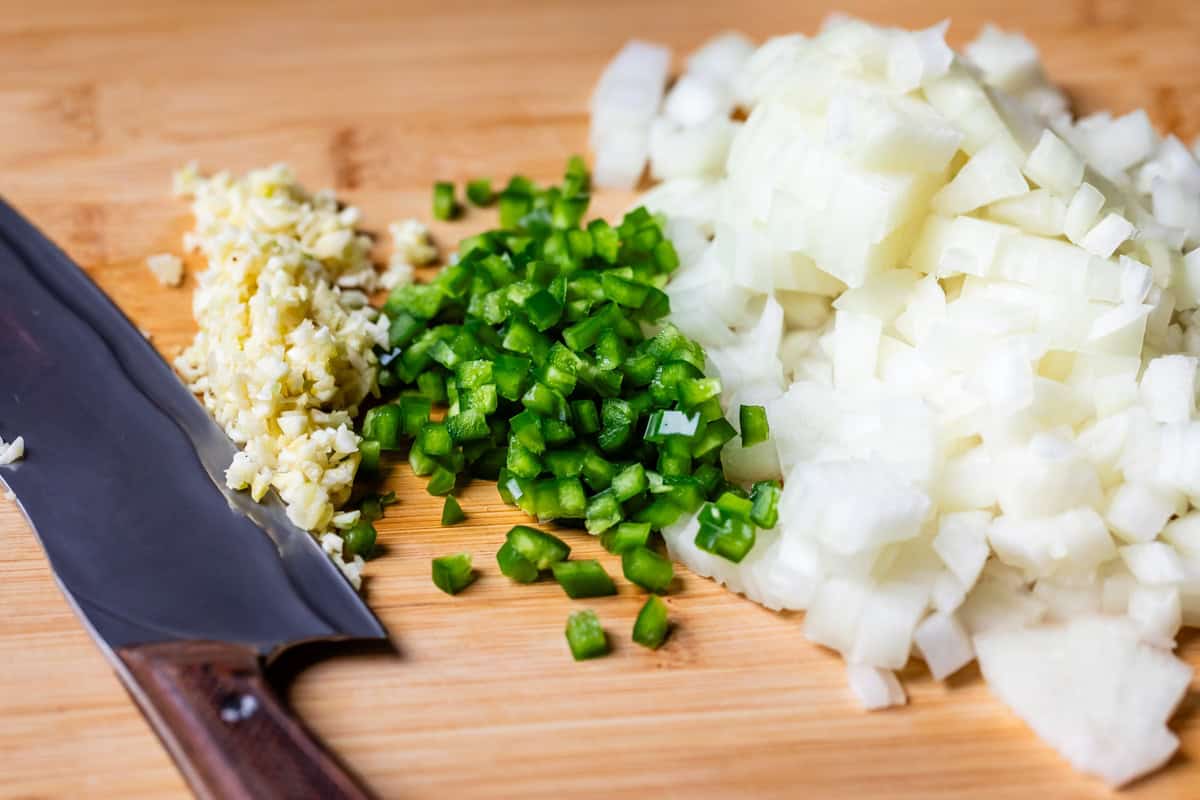 diced onion, jalapeno, and garlic on a wooden cutting board.