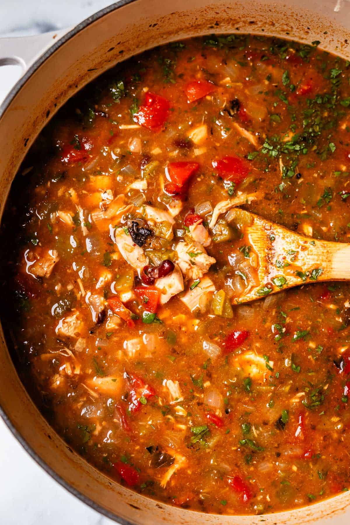 looking down into a finished pot of chicken tortilla soup with a wooden spoon in it.