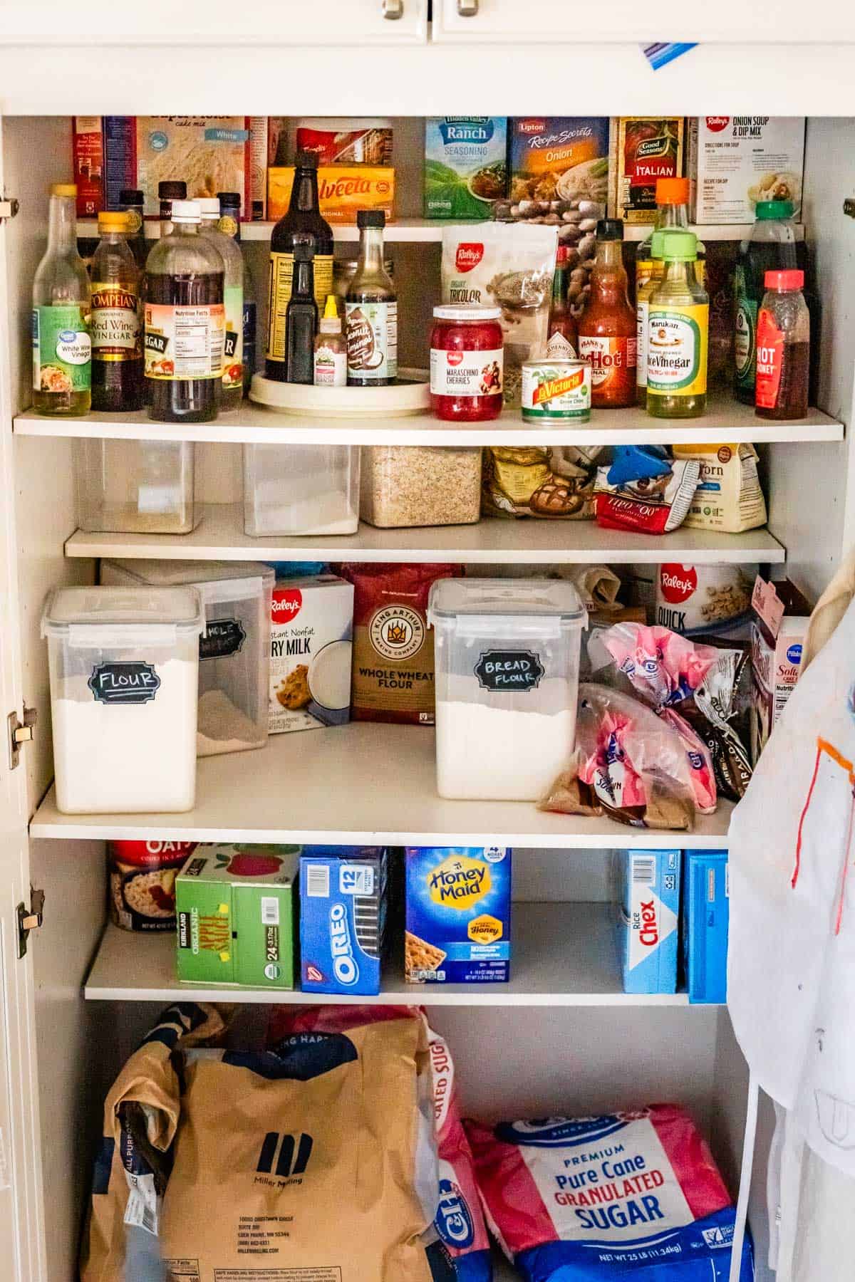 pantry open to show shelves of flour, sugar, vinegar, maraschino cherries, honey, brown sugar, etc.