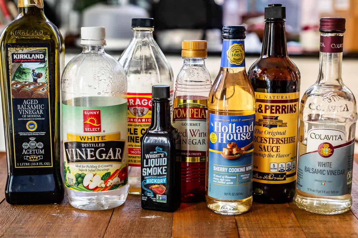 Vinegar, liquid smoke, cooking wine, and Worcestershire sauce lined up on a wood table.