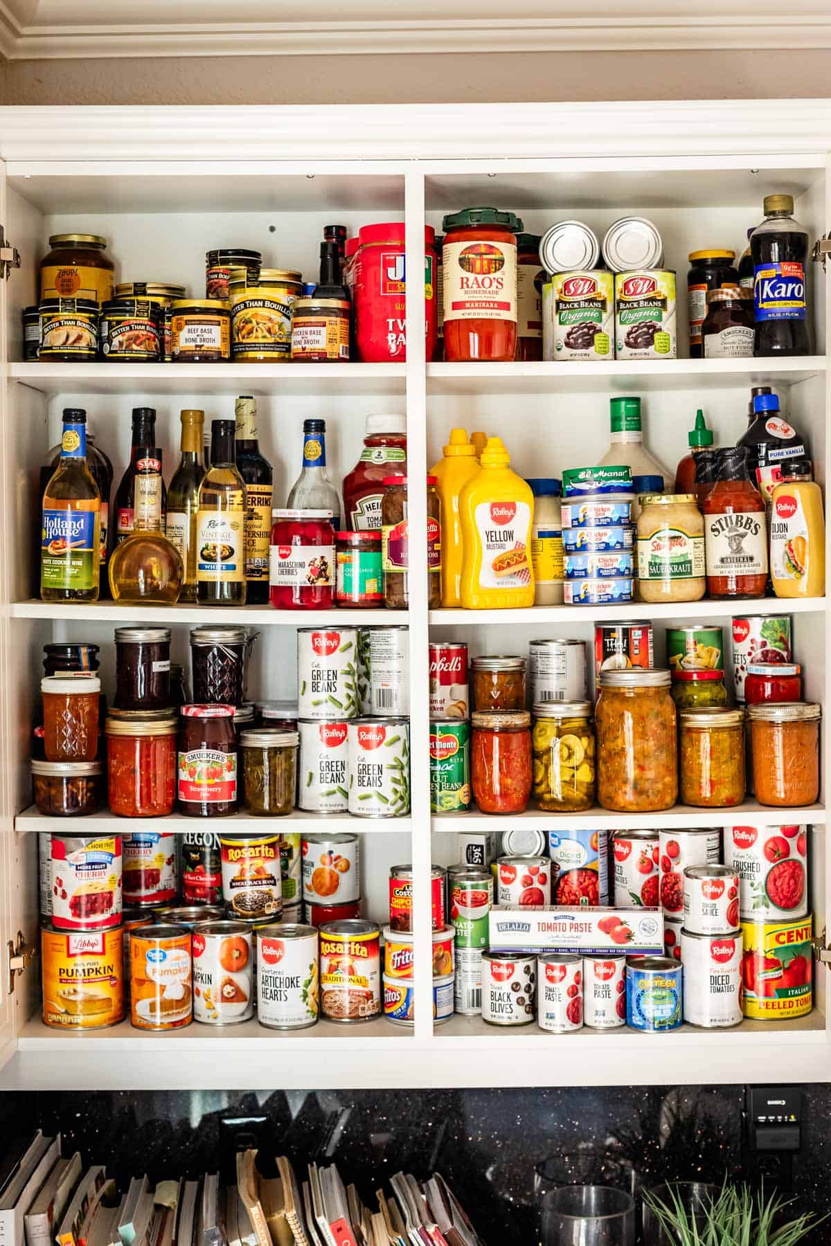 picture of white cupboards open to show pantry items like mustard, canned goods, pasta sauce, vinegar, etc.
