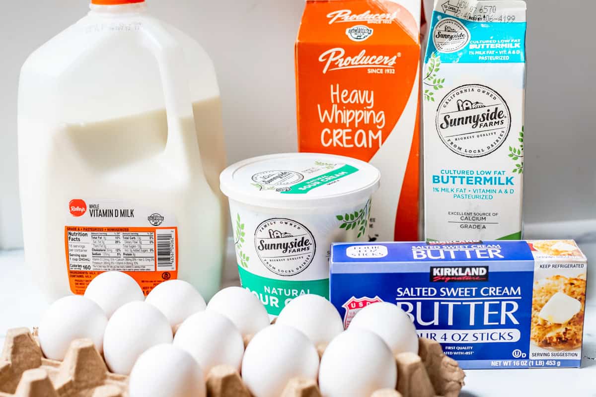 Milk, sour cream, whipping cream, buttermilk, butter, and eggs on a white surface.