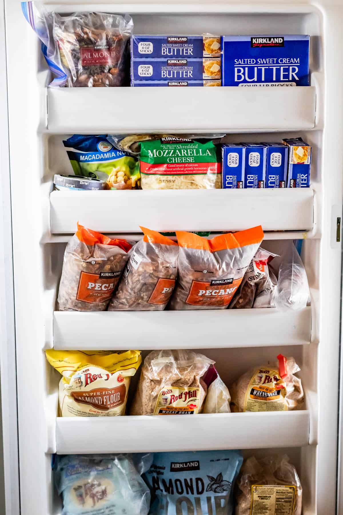 Door of a freezer with lots of butter, pecans, cheese, almond flour, macadamia nuts, and other freezer items.