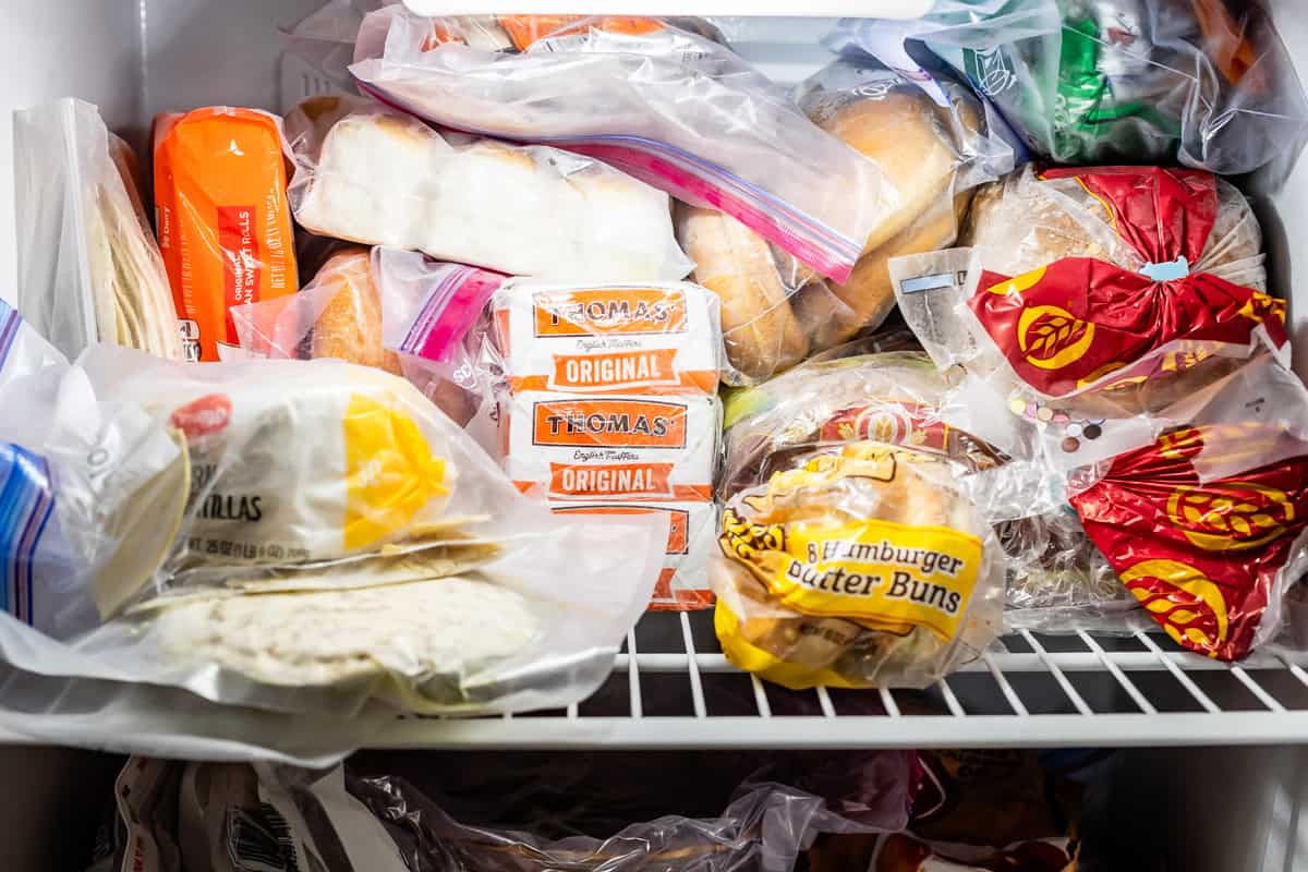 Top shelf of a freezer with frozen bread, rolls, tortillas, and hamburger buns.