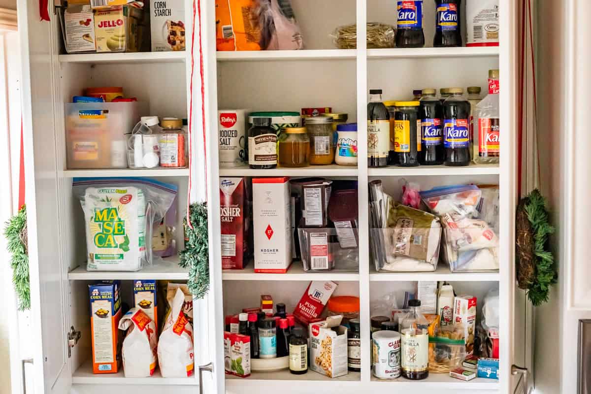 pantry cupboards open to show vanilla, cornstarch, Maseca, karo syrup, extracts, baking powder, etc.