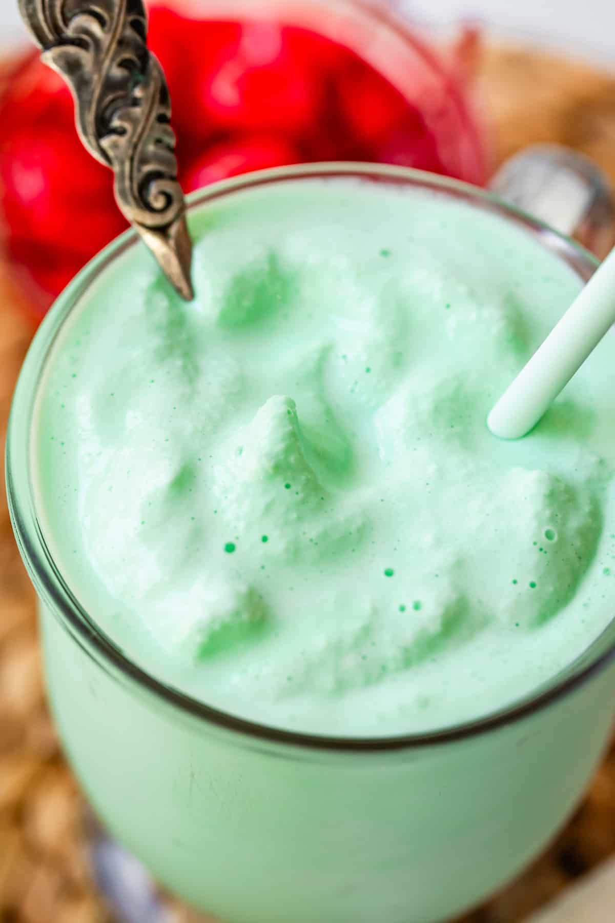 glass mug with shamrock shake with a spoon and a straw in it.