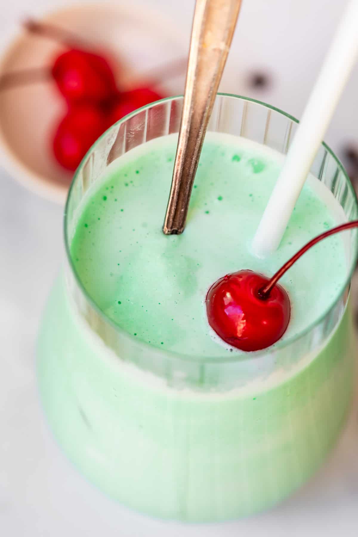 looking into a glass cup with shamrock shake, a spoon, a straw, and a cherry.