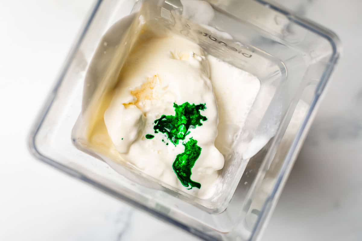 looking down into blender showing green food coloring on top of vanilla ice cream.