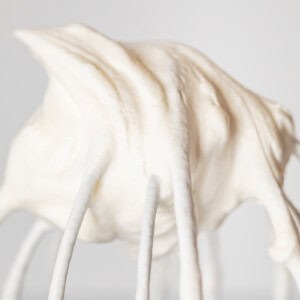 close up of whipped cream in a stiff peak on a whisk attachment.