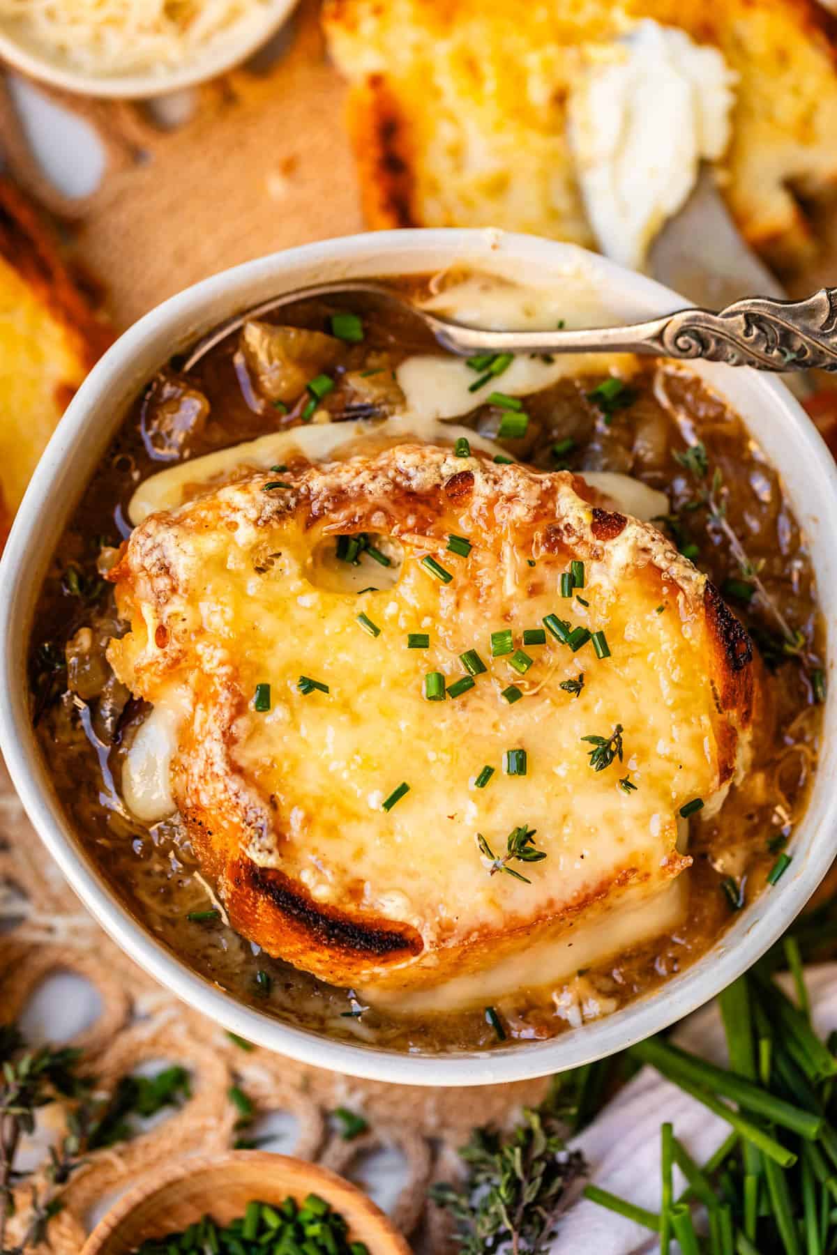 spoon in a stoneware bowl of french onion soup with toasty bread and cheese.