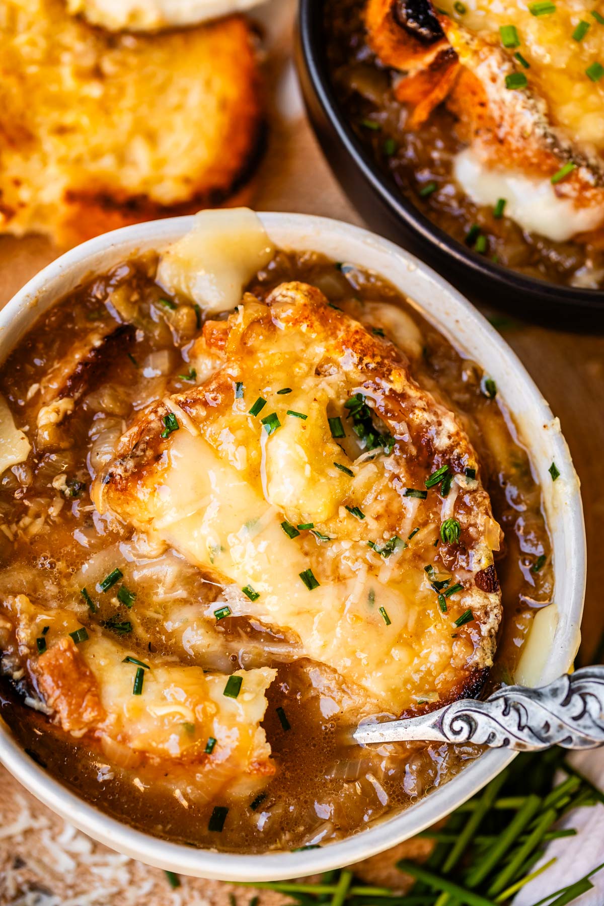 spoon stuck into a stoneware bowl with french onion soup with bread and cheese.