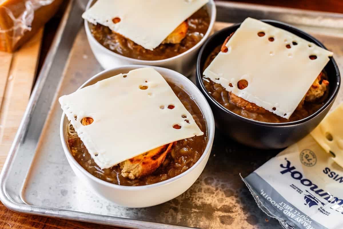 three bowls filled with french onion soup, topped with bread and cheese ready to be toasted.
