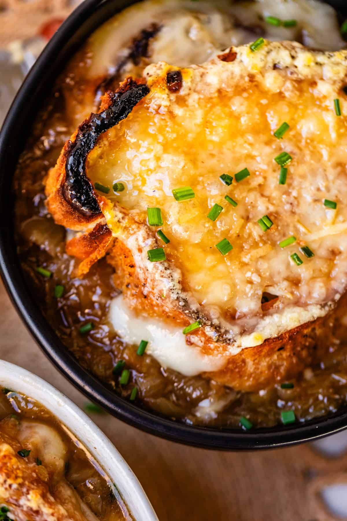 close up of toasty baguette with cheese on top of a bowl of french onion soup.