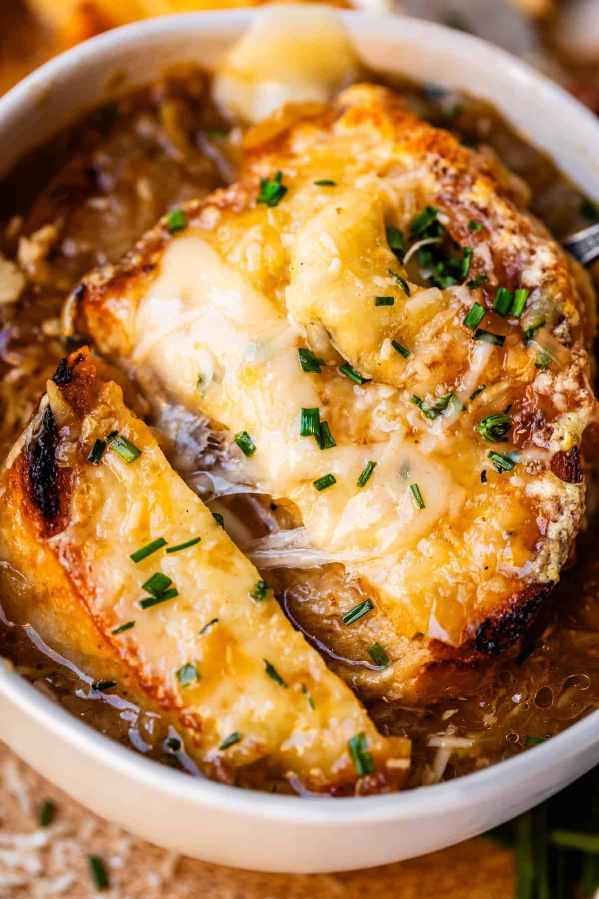 close up of toasty baguette with cheese on top of a bowl of french onion soup.