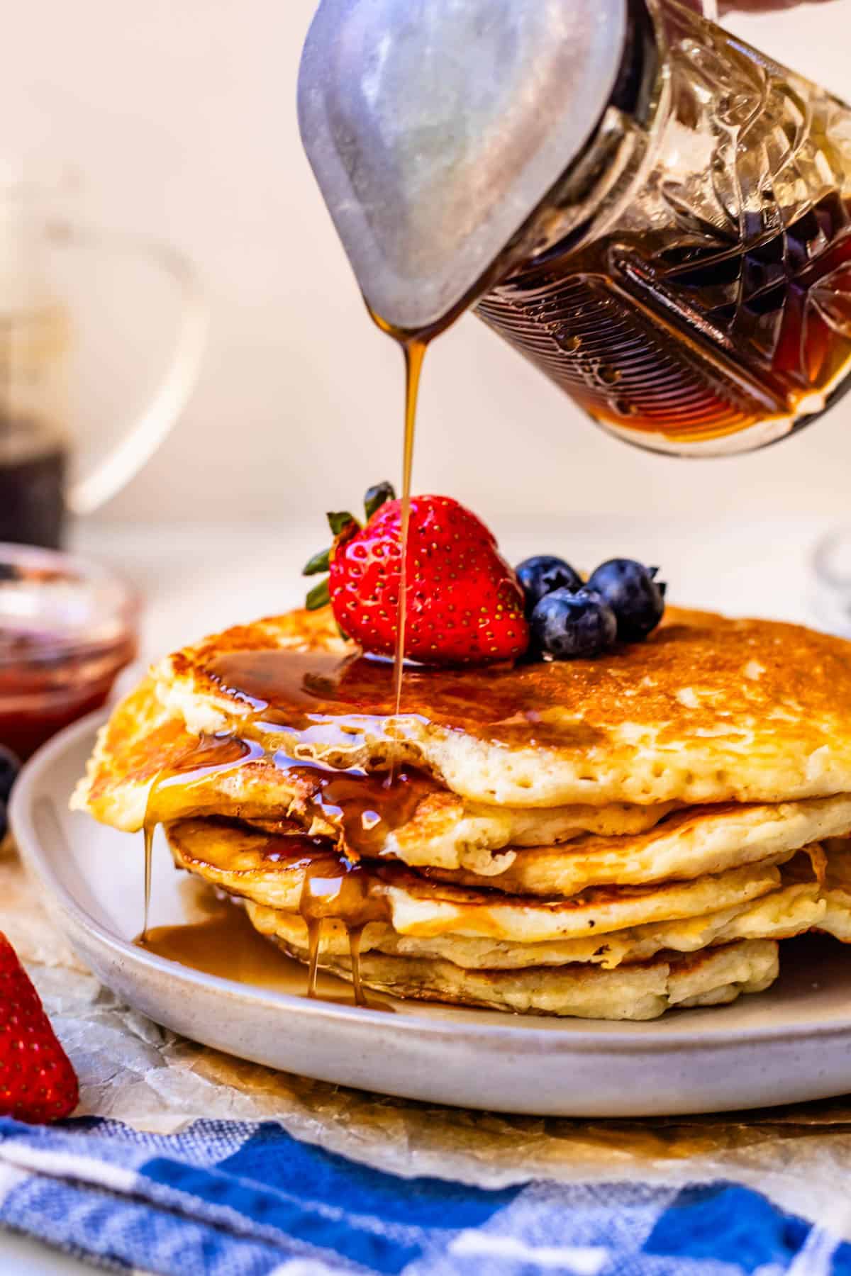 homemade syrup being poured on a stack of pancakes with fresh berries.