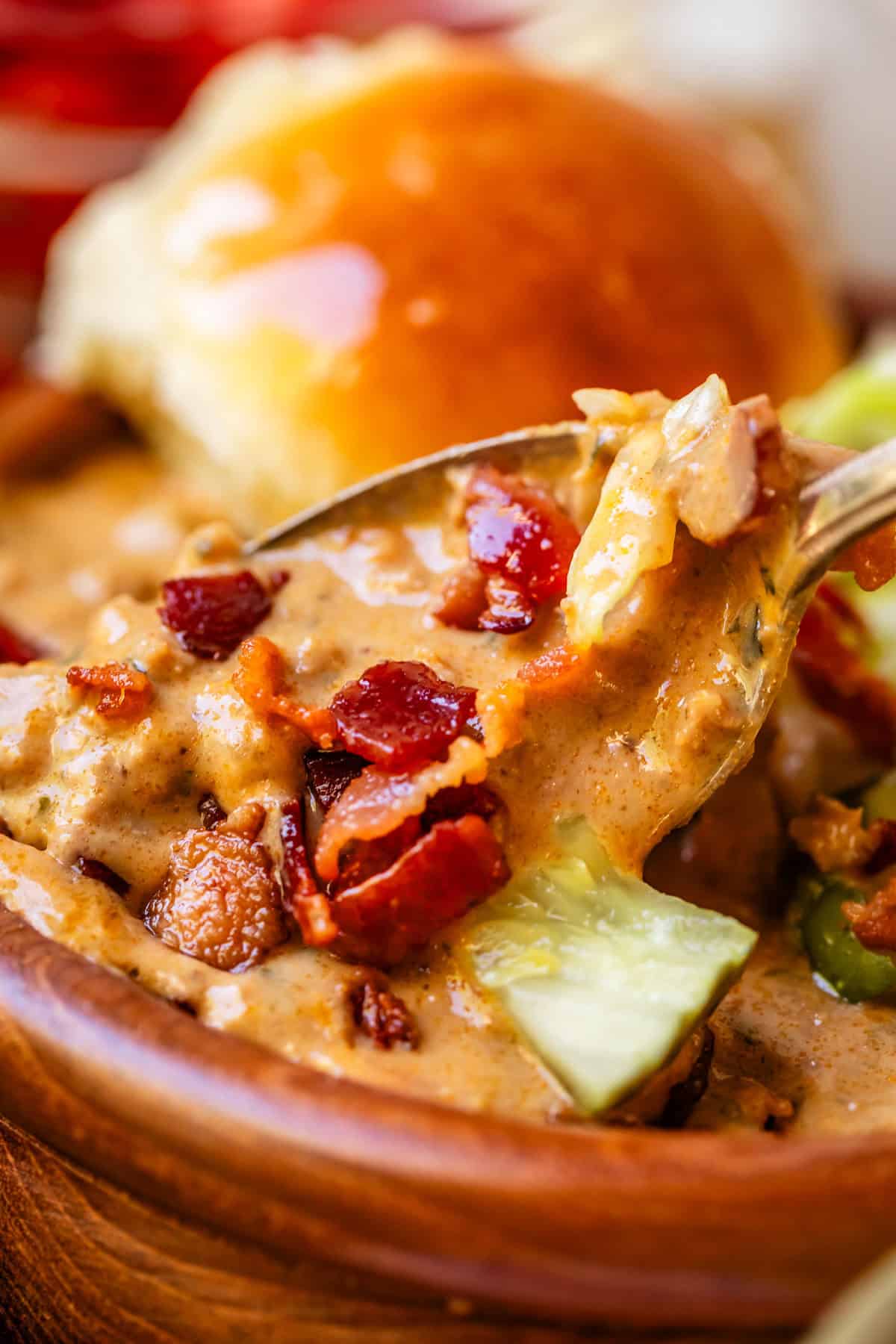 close up shot of a spoon lifting a bite of cheeseburger soup with a buttered bun in the background.