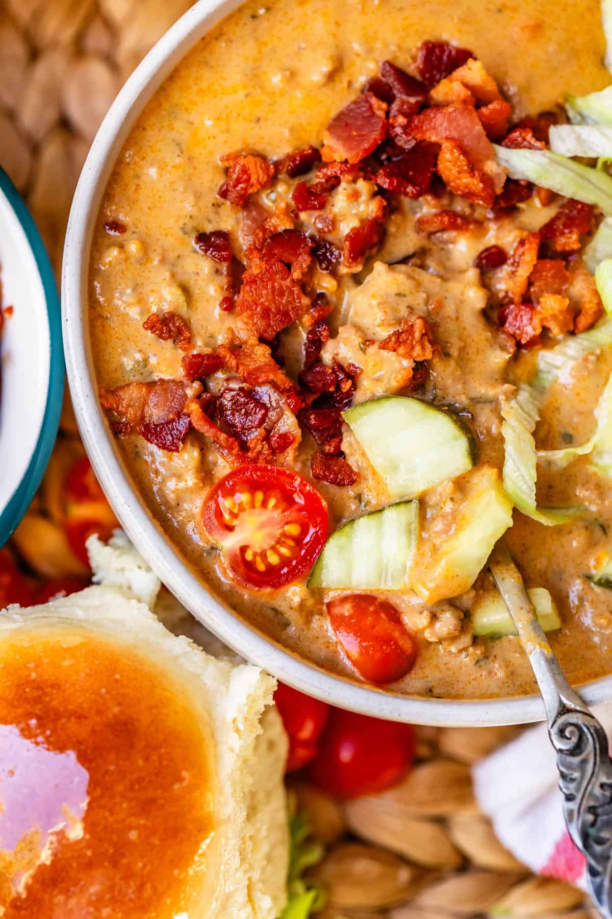cheeseburger soup topped with lettuce, pickles, onions, and bacon with a buttery dinner roll.