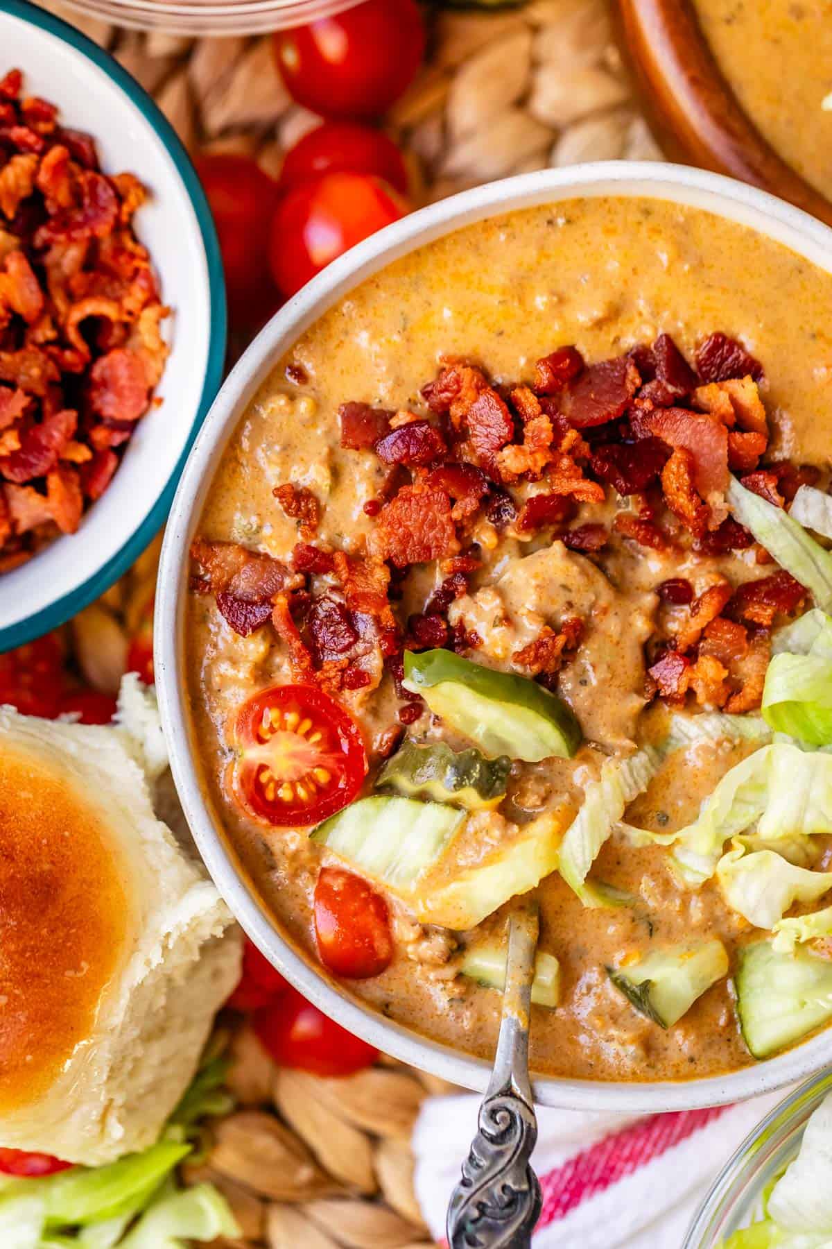 cheeseburger soup with a spoon it in and a soft dinner roll nearby.