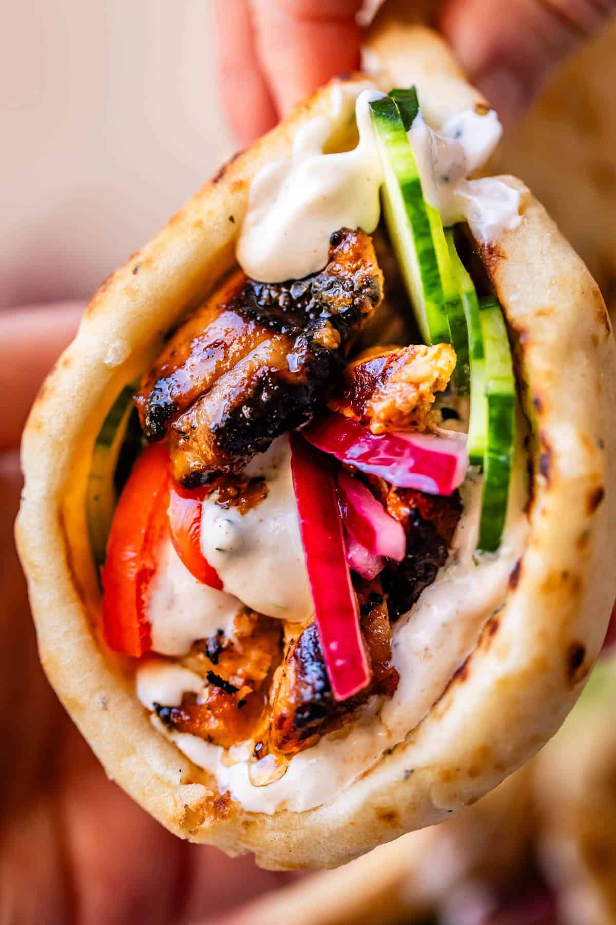 hand holding chicken shawarma in naan with cucumber, onion, and garlic sauce.