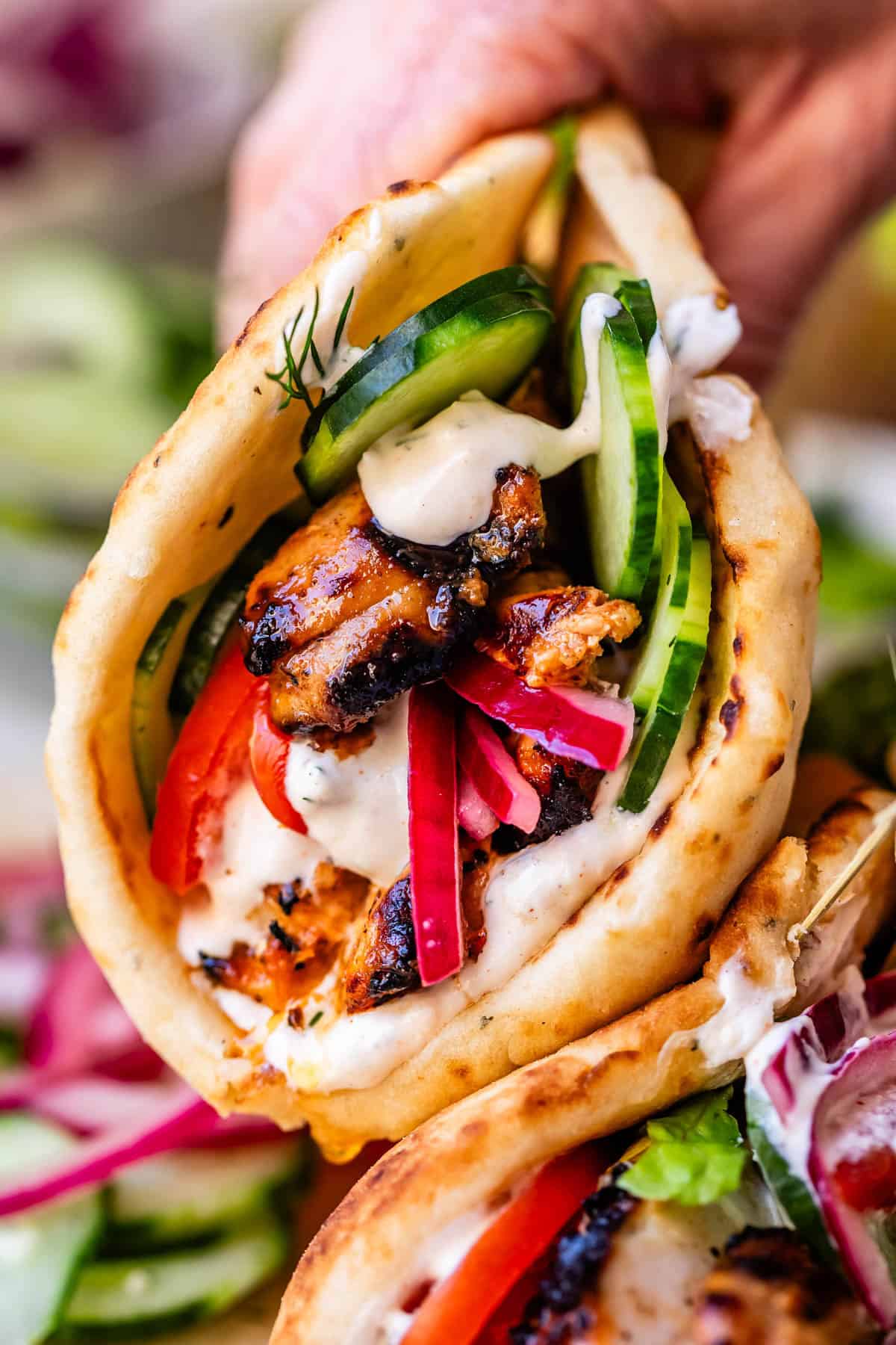 hand holding chicken shawarma in naan with cucumber, onion, and garlic sauce.