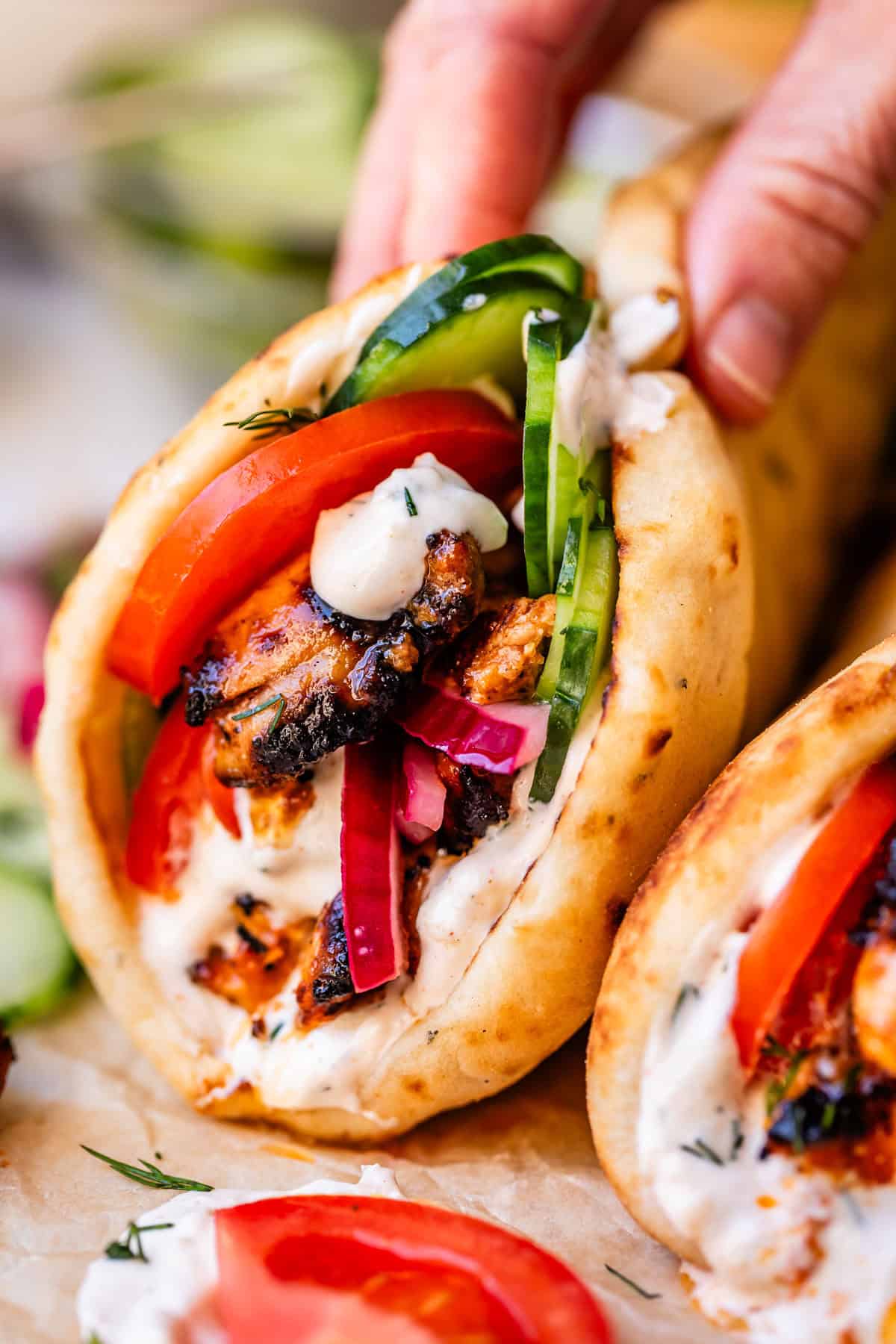 hand holding a chicken shawarma wrap with all the fixings and sitting on parnchment.