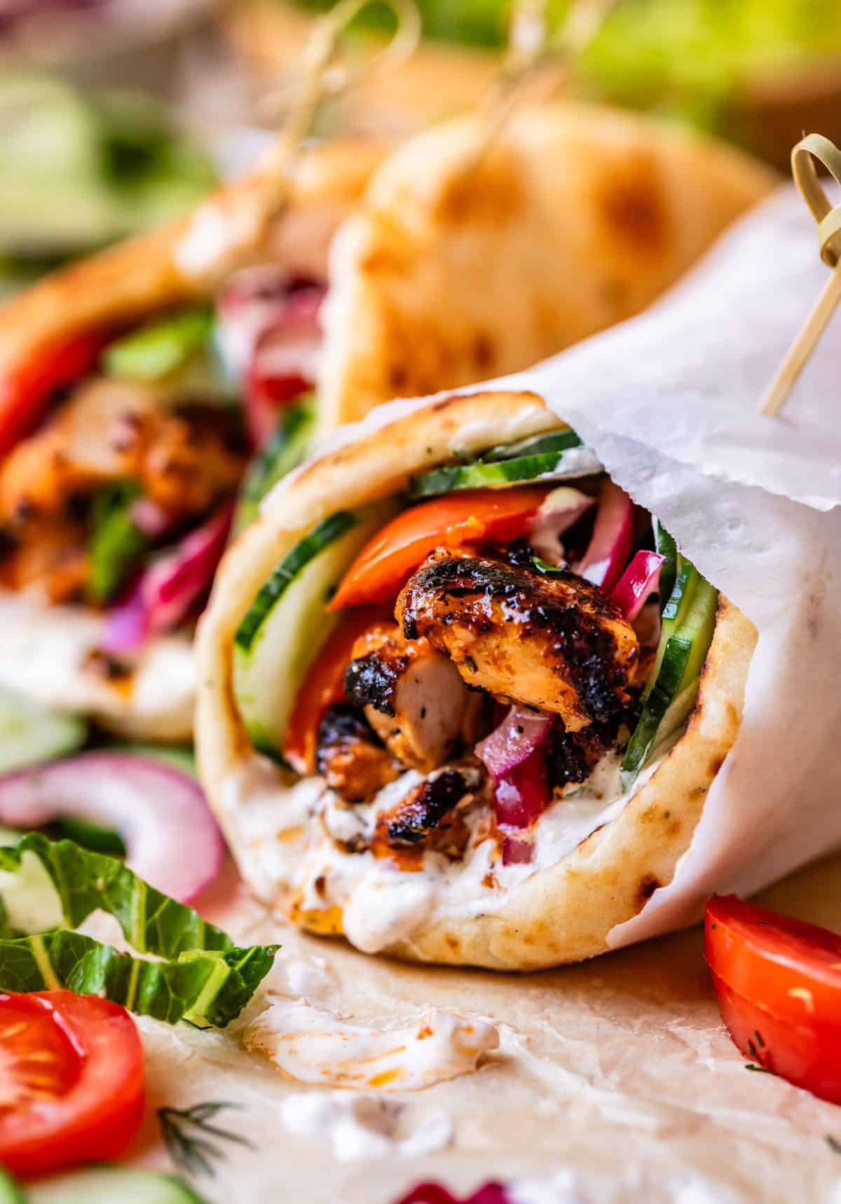 parchment paper wrapped chicken shawarma layered with tomato and cucumber in naan.