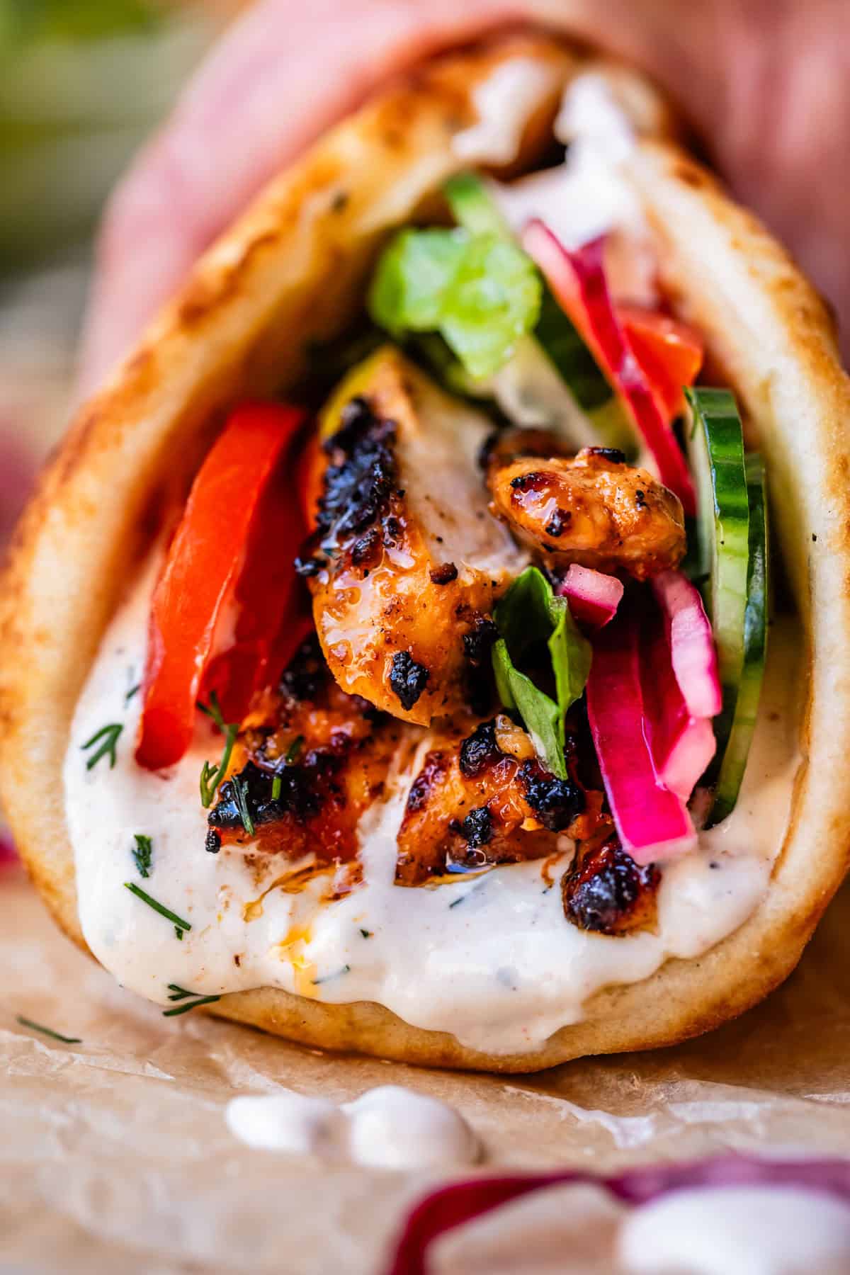 hand holding chicken shawarma in naan with cucumber, onion, and garlic sauce.