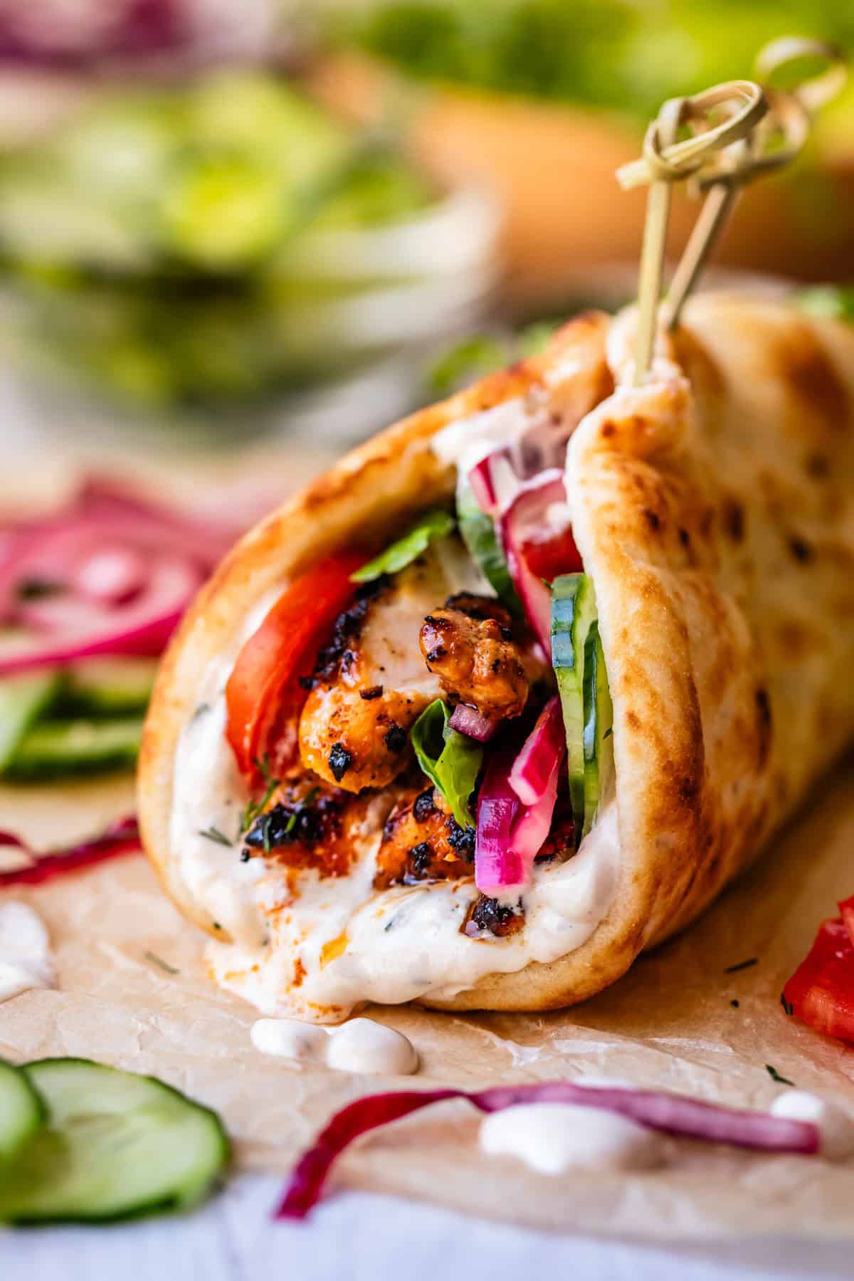 chicken shawarma in naan with cucumber, onion, and garlic sauce on parchment paper.