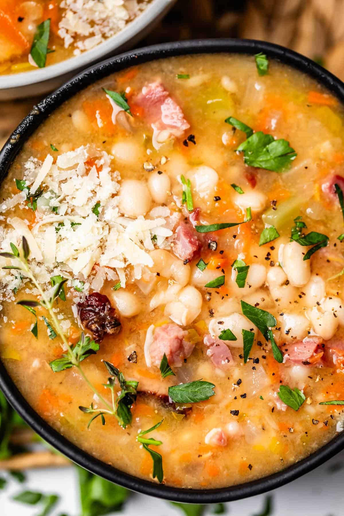 close up looking at ham and bean soup with garnish like cheese, parsley, and pepper.