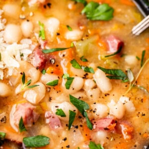 close up looking at ham and bean soup with garnish like cheese, parsley, and pepper.