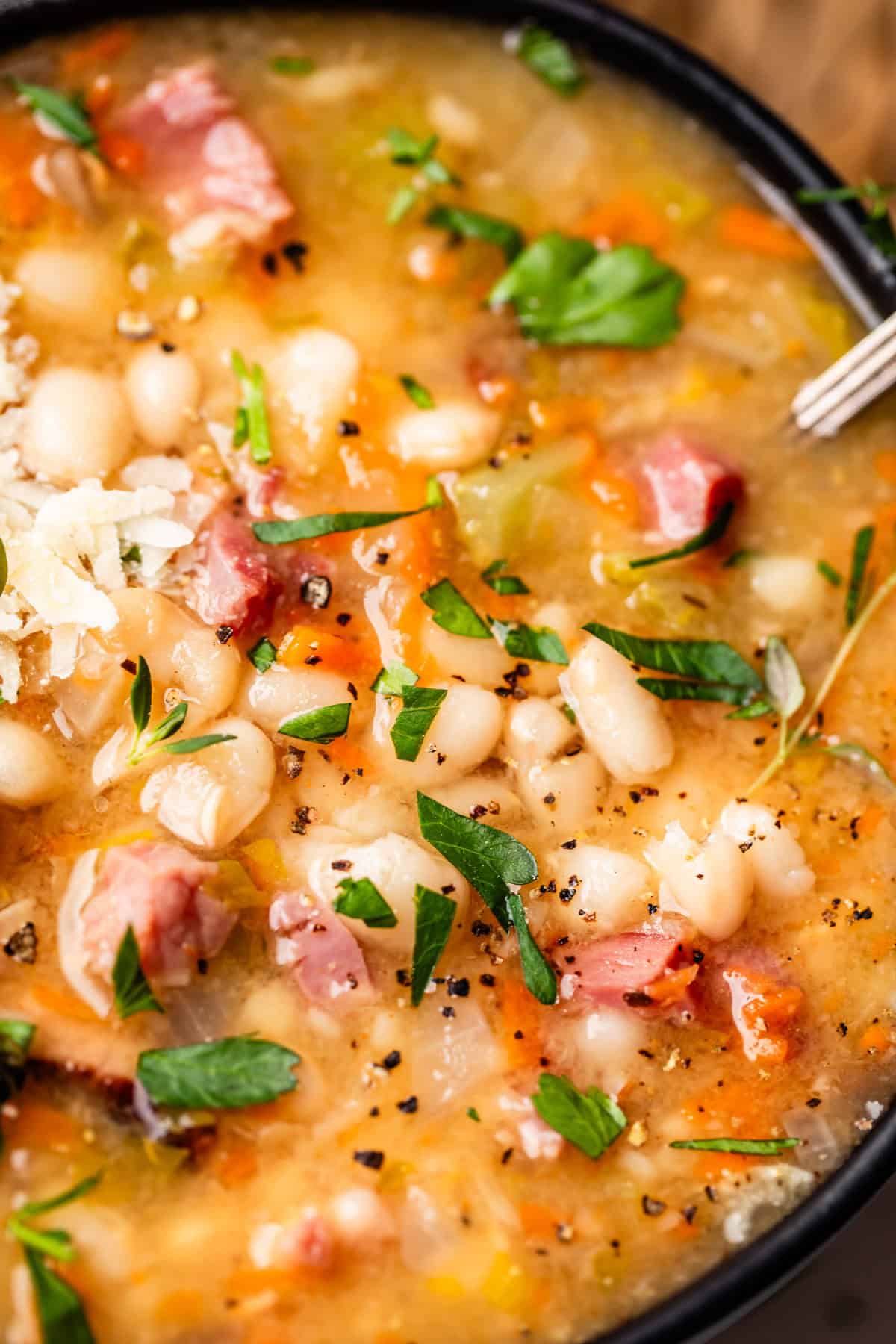 close up looking at ham and bean soup with garnish like cheese, parsley, and pepper.