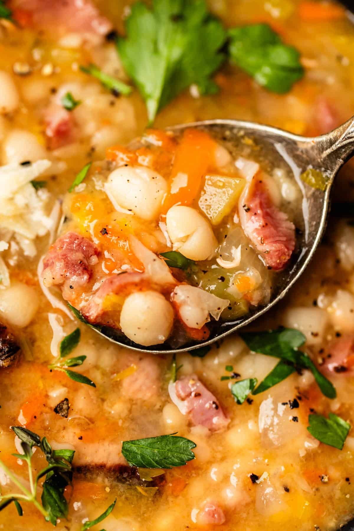 metal spoon holding a bite of ham and bean soup over a bowl filled with the same.
