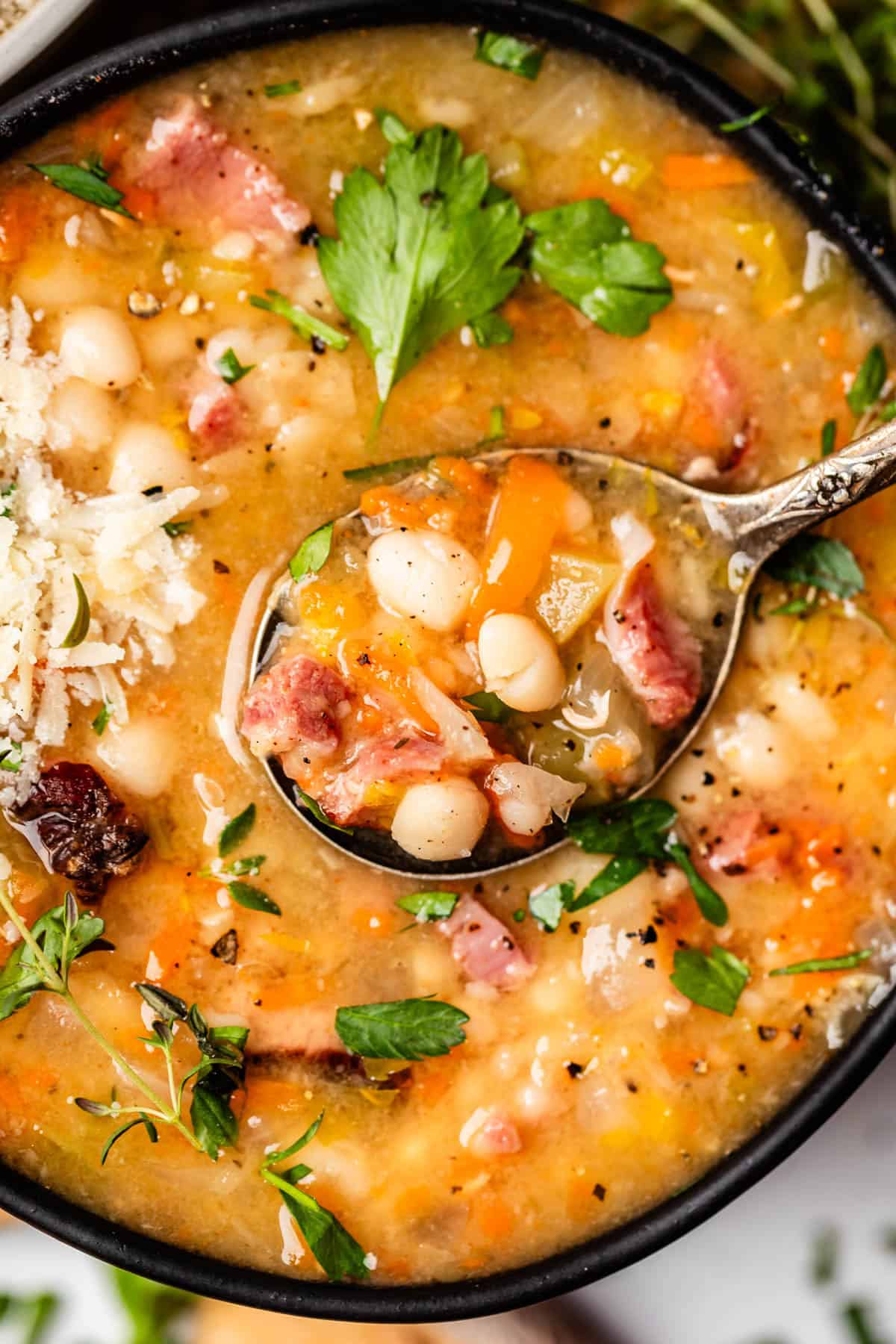 metal spoon holding a bite of ham and bean soup over a bowl filled with the same.