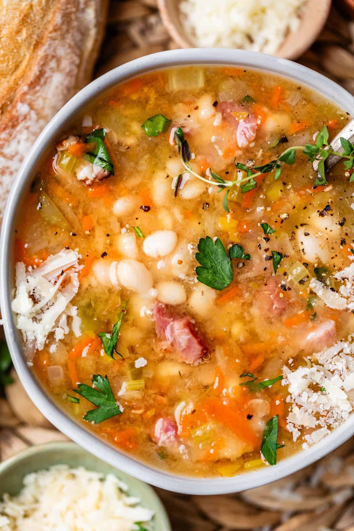 ceramic bowl filled with ham & bean soup, garnished with parmesan, parsley, and pepper.